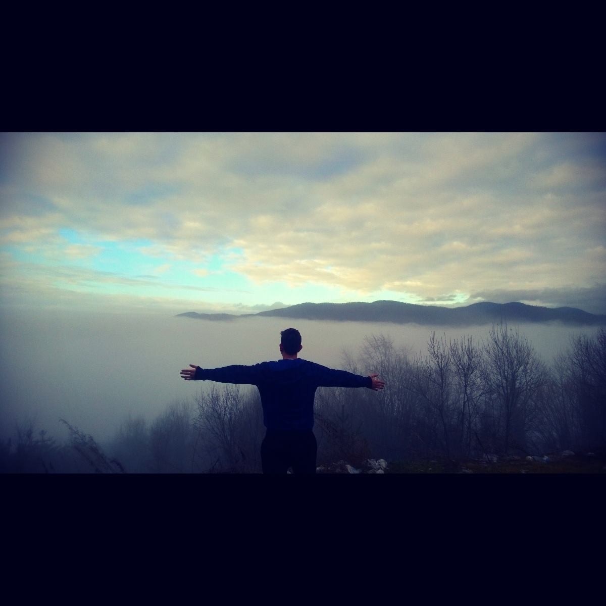 Man with arms outstretched overlooking misty mountains HD Wallpaper