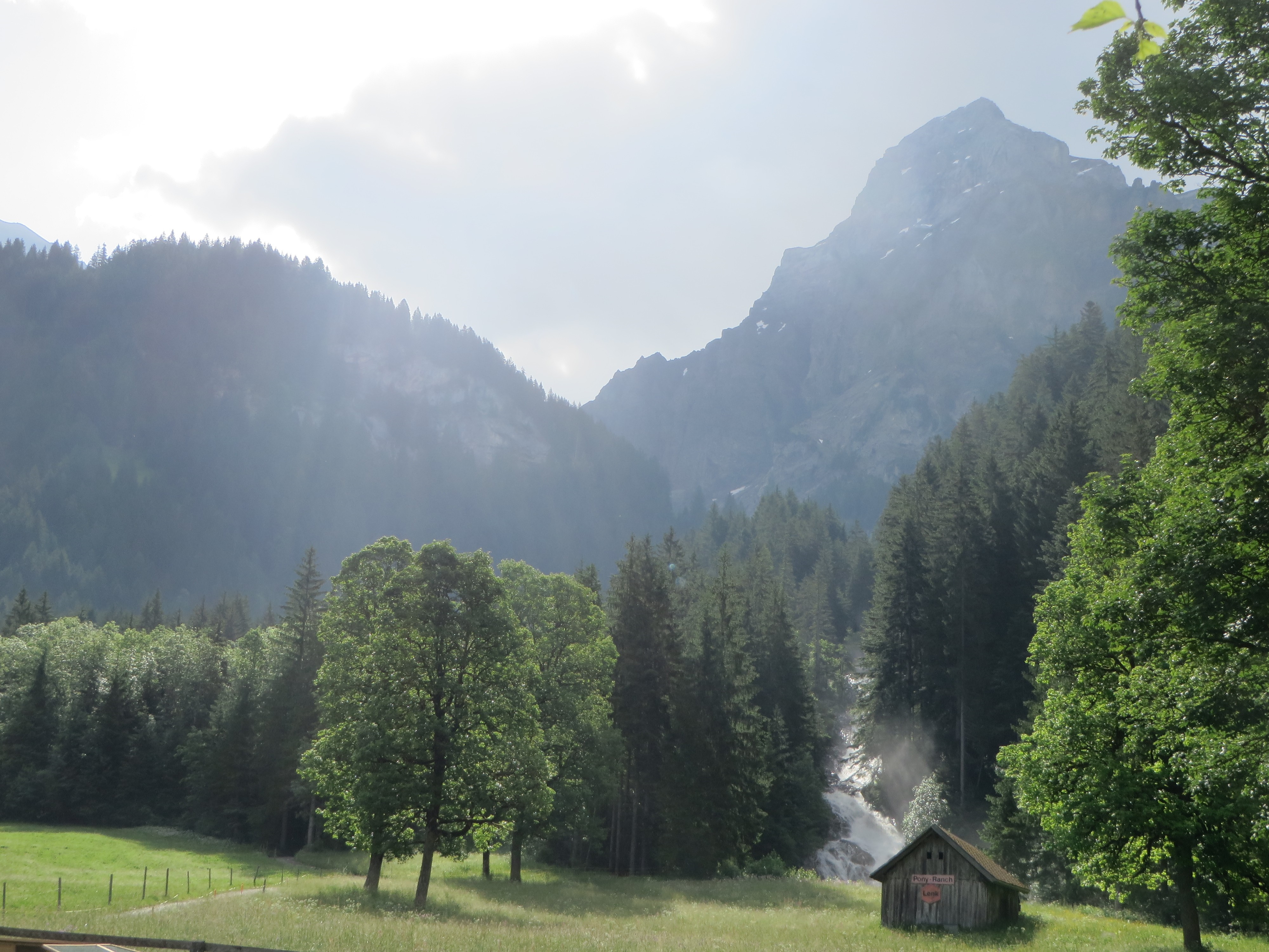 Wooden shack in a mountain valley with a waterfall HD Wallpaper