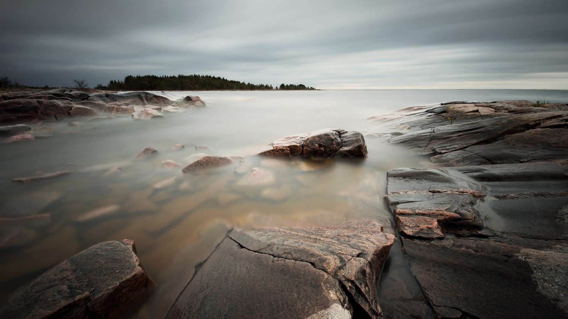 Rocky shoreline with calm water and cloudy sky HD Wallpaper