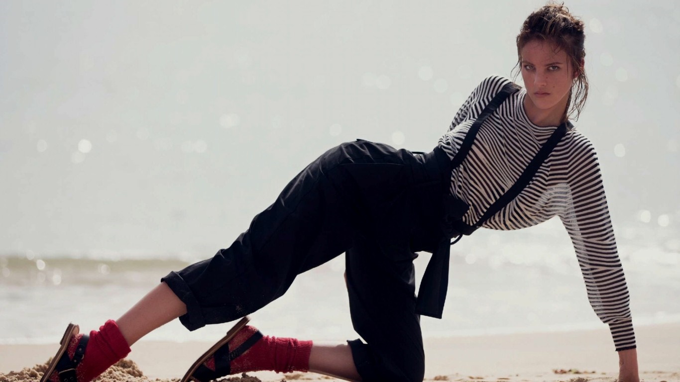 Eliza Cummings on a beach in black overalls and striped shirt HD Wallpaper