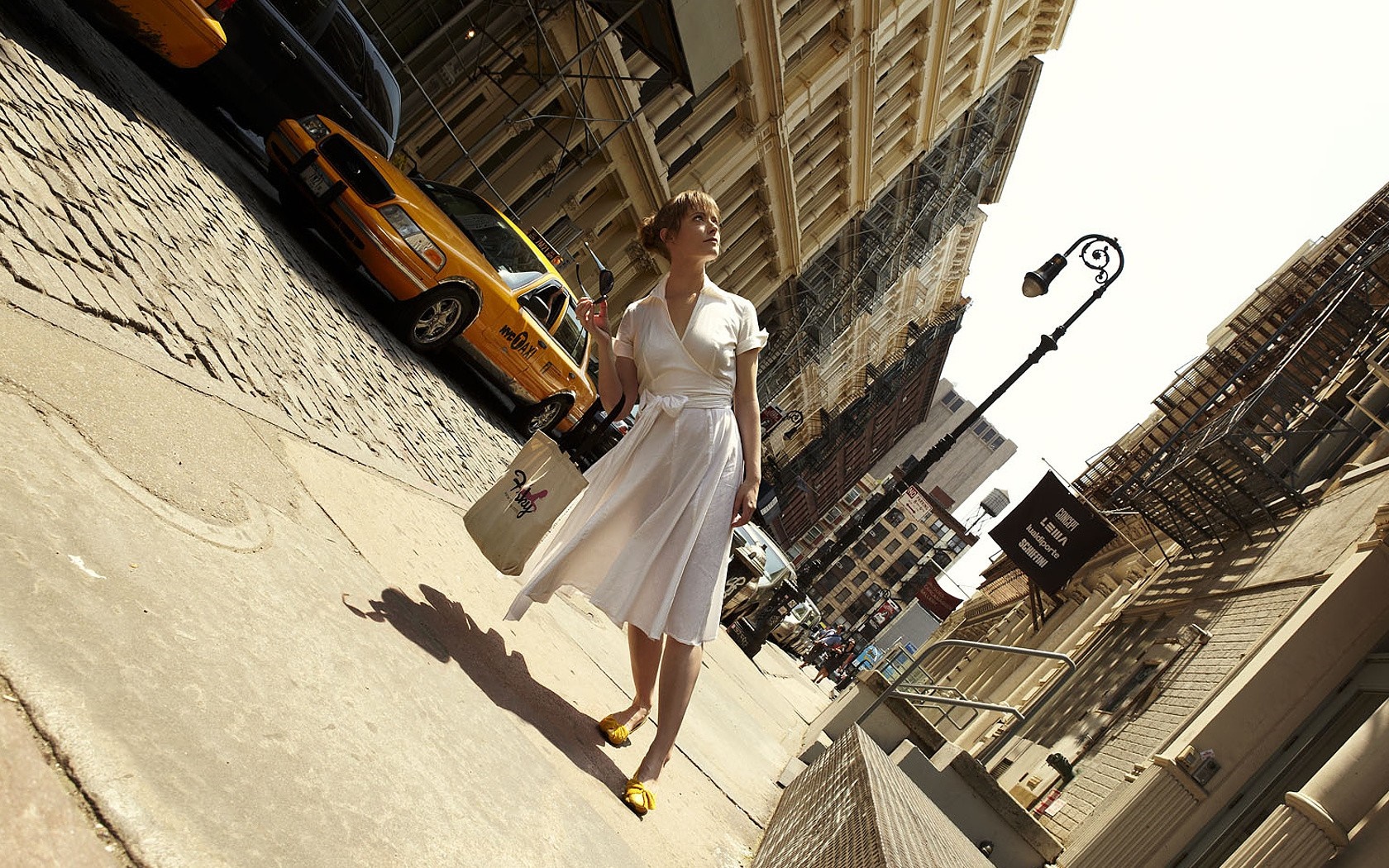 Woman in white dress walking on cobblestone street with yellow taxi HD Wallpaper