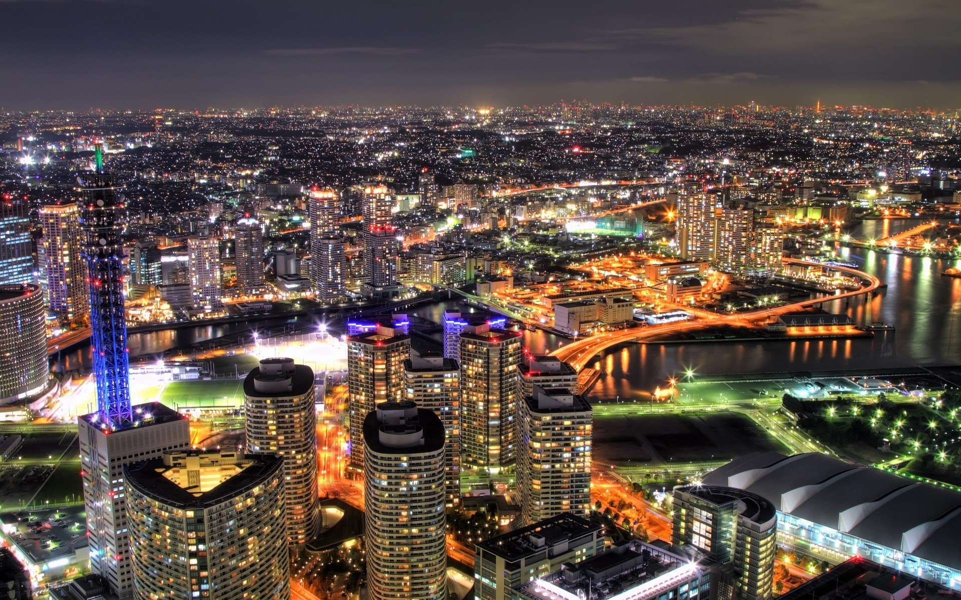 Cityscape at night with illuminated skyscrapers and a river HD Wallpaper