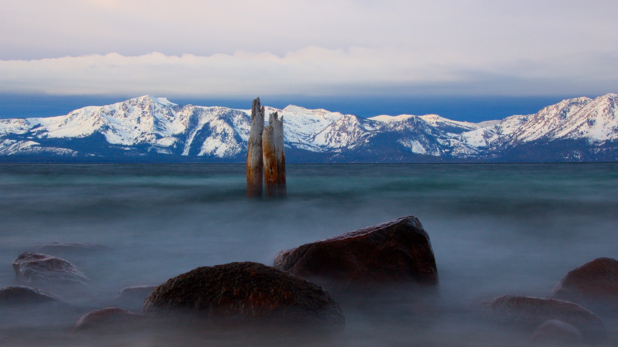 Snowy mountains over a misty lake with rocks HD Wallpaper