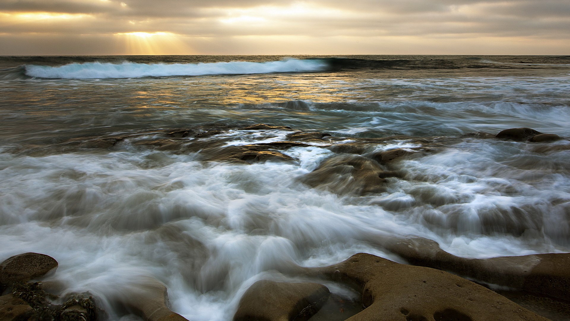Ocean waves crashing on rocky shore at sunset HD Wallpaper