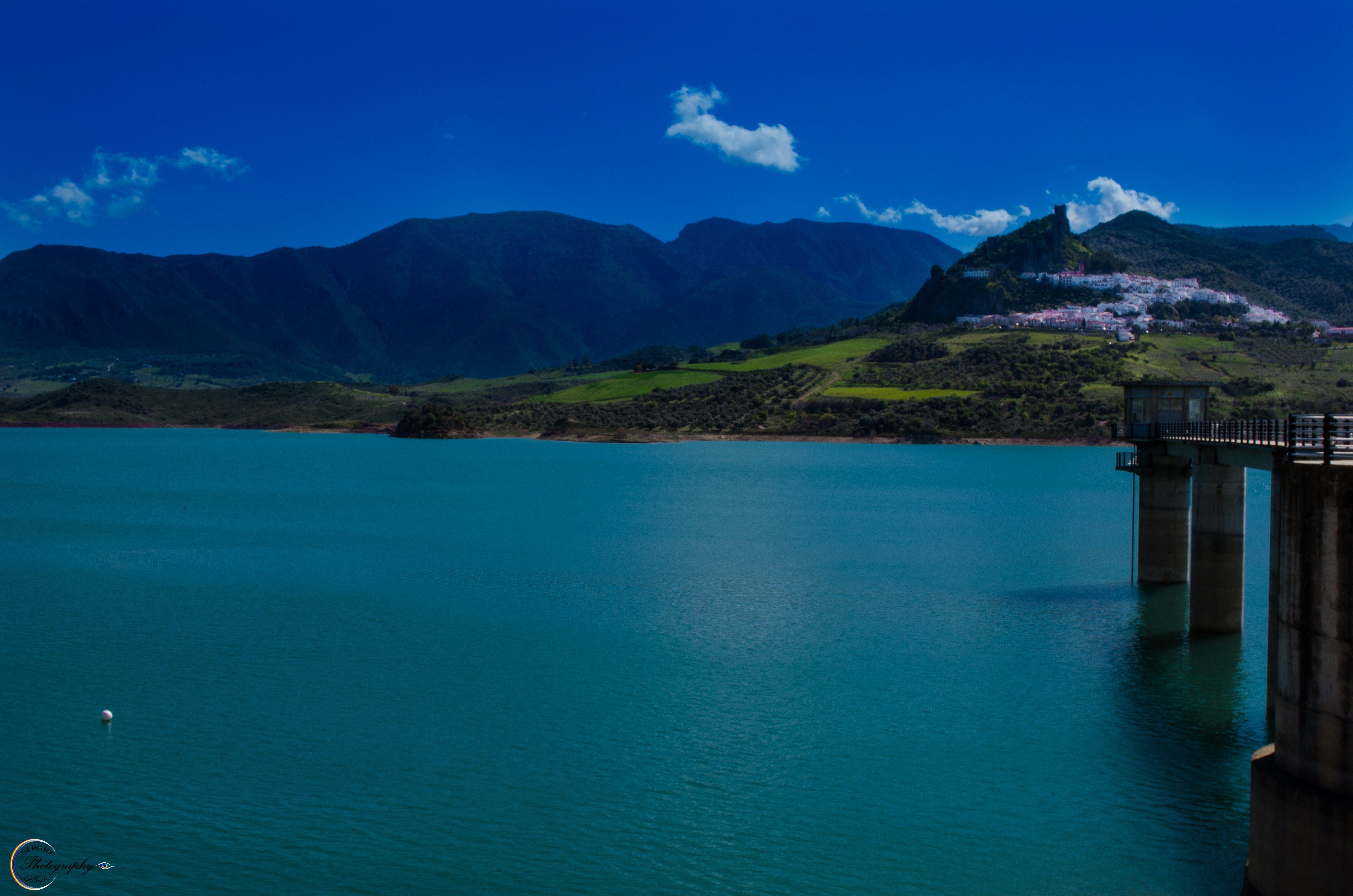 Reservoir with mountains and a white village on a hill HD Wallpaper