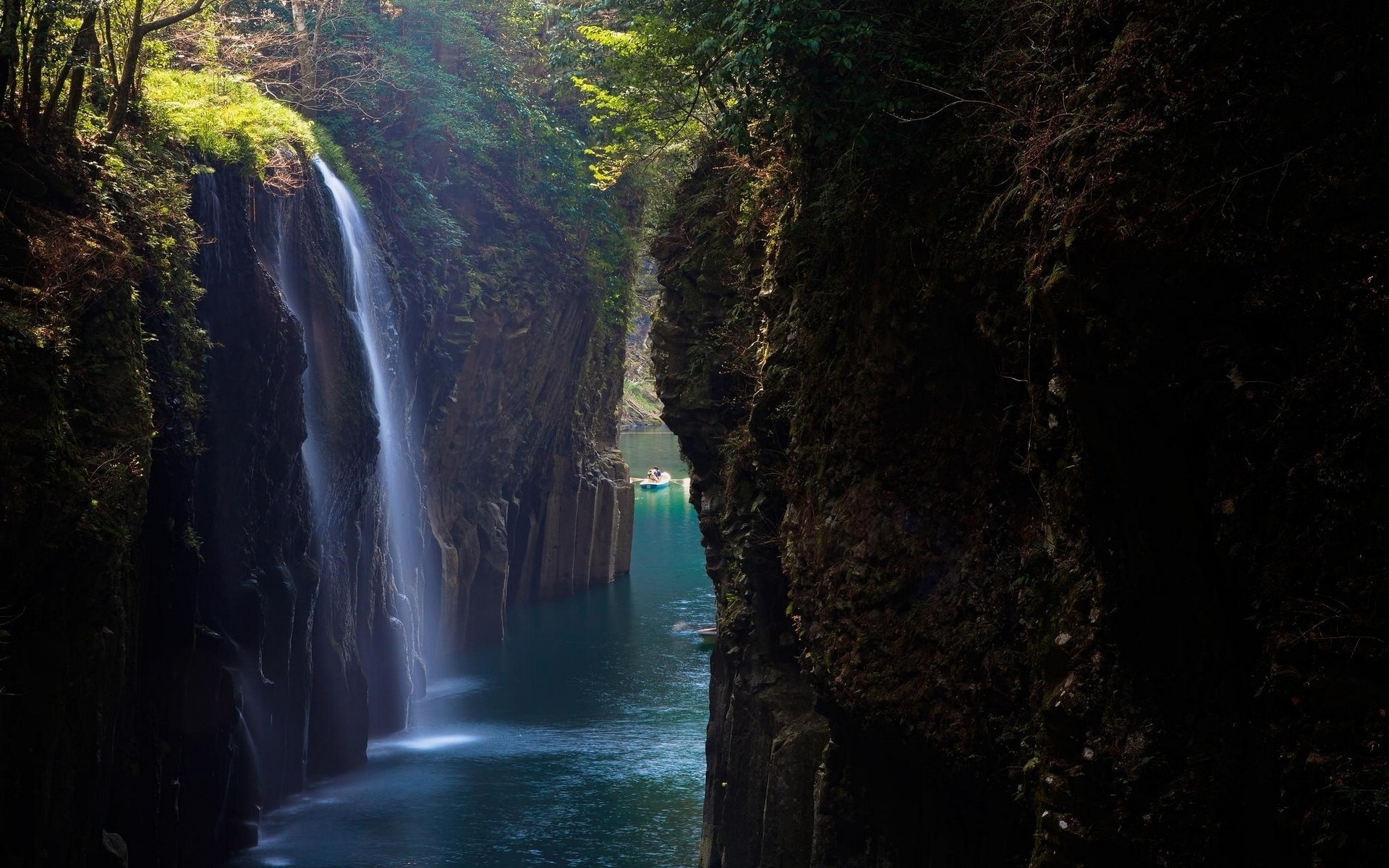 Waterfall flowing into a river canyon with a boat HD Wallpaper