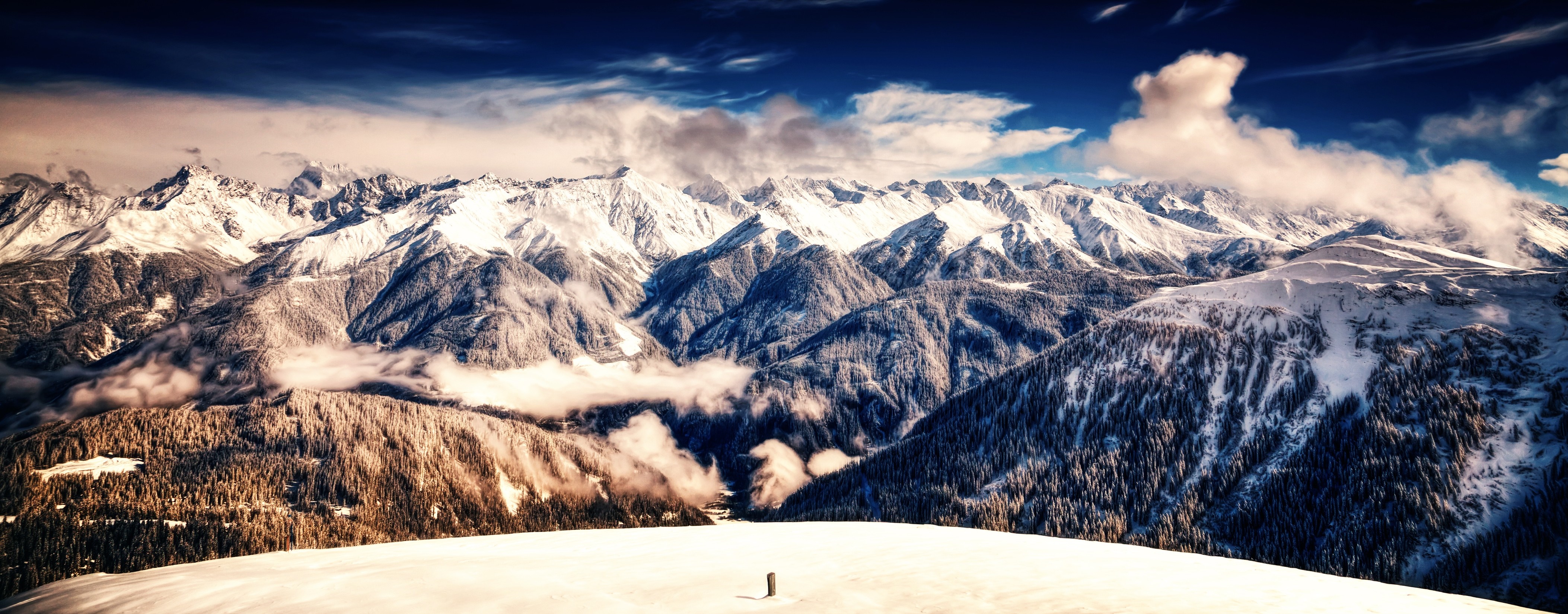 Snow-covered mountains and forests under a cloudy sky HD Wallpaper