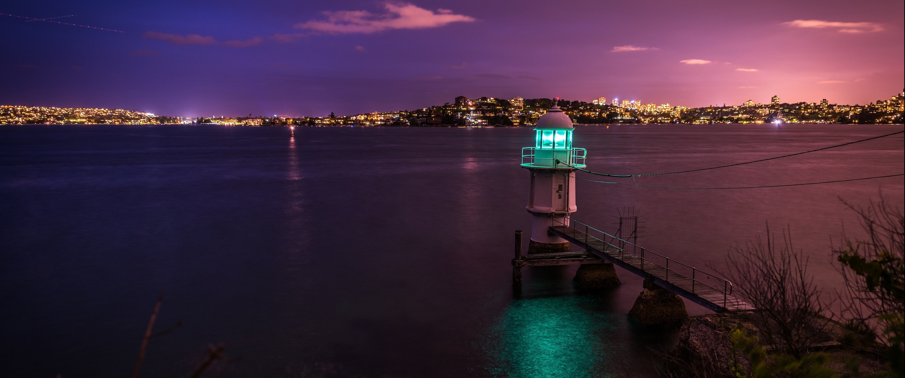 Lighthouse on the water at dusk with city lights HD Wallpaper