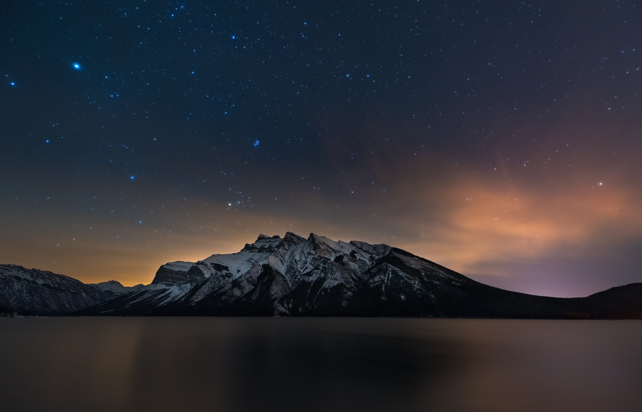 Snowy mountains reflected in a lake under a starry night sky HD Wallpaper