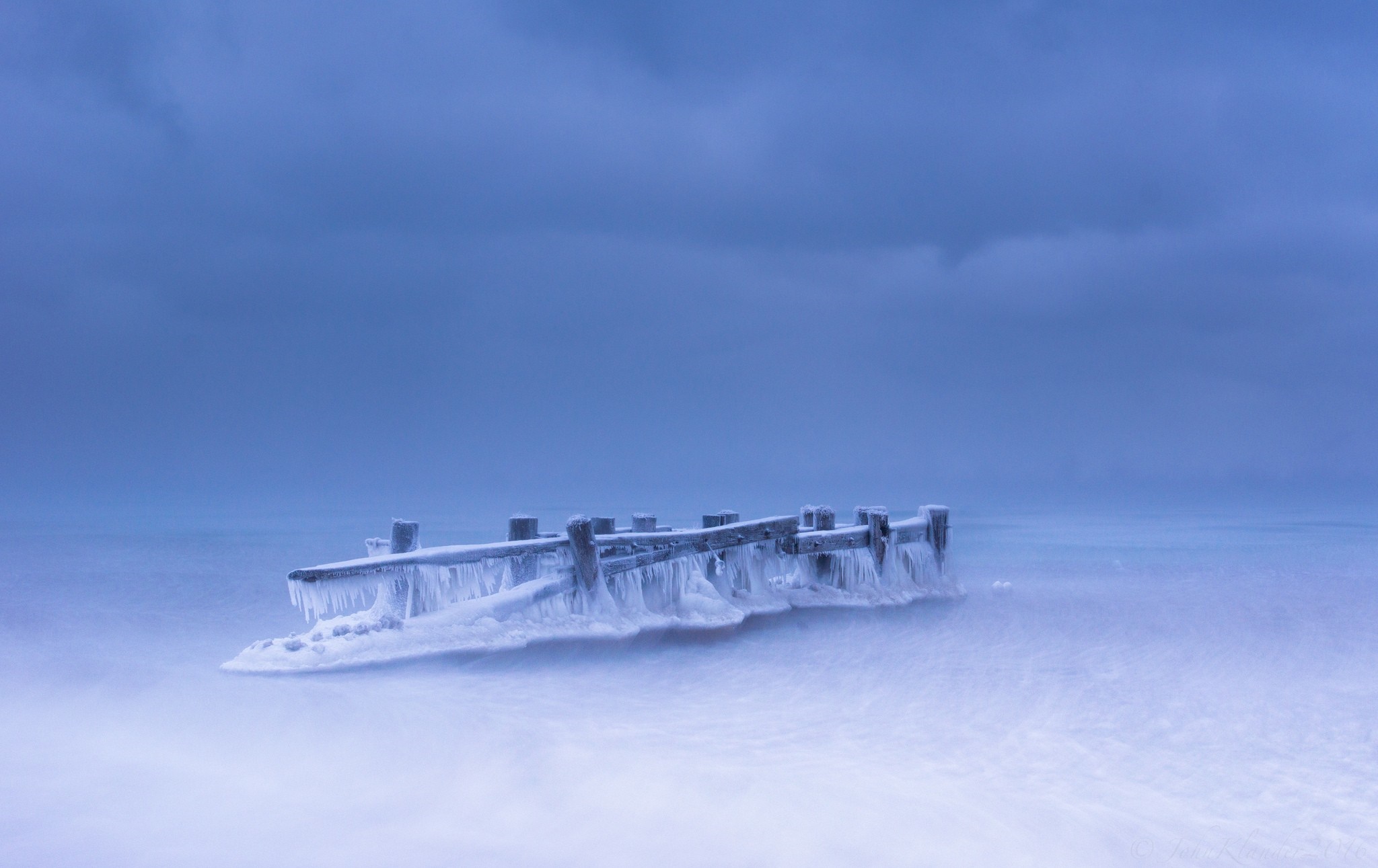 Frozen pier in icy water under cloudy sky HD Wallpaper