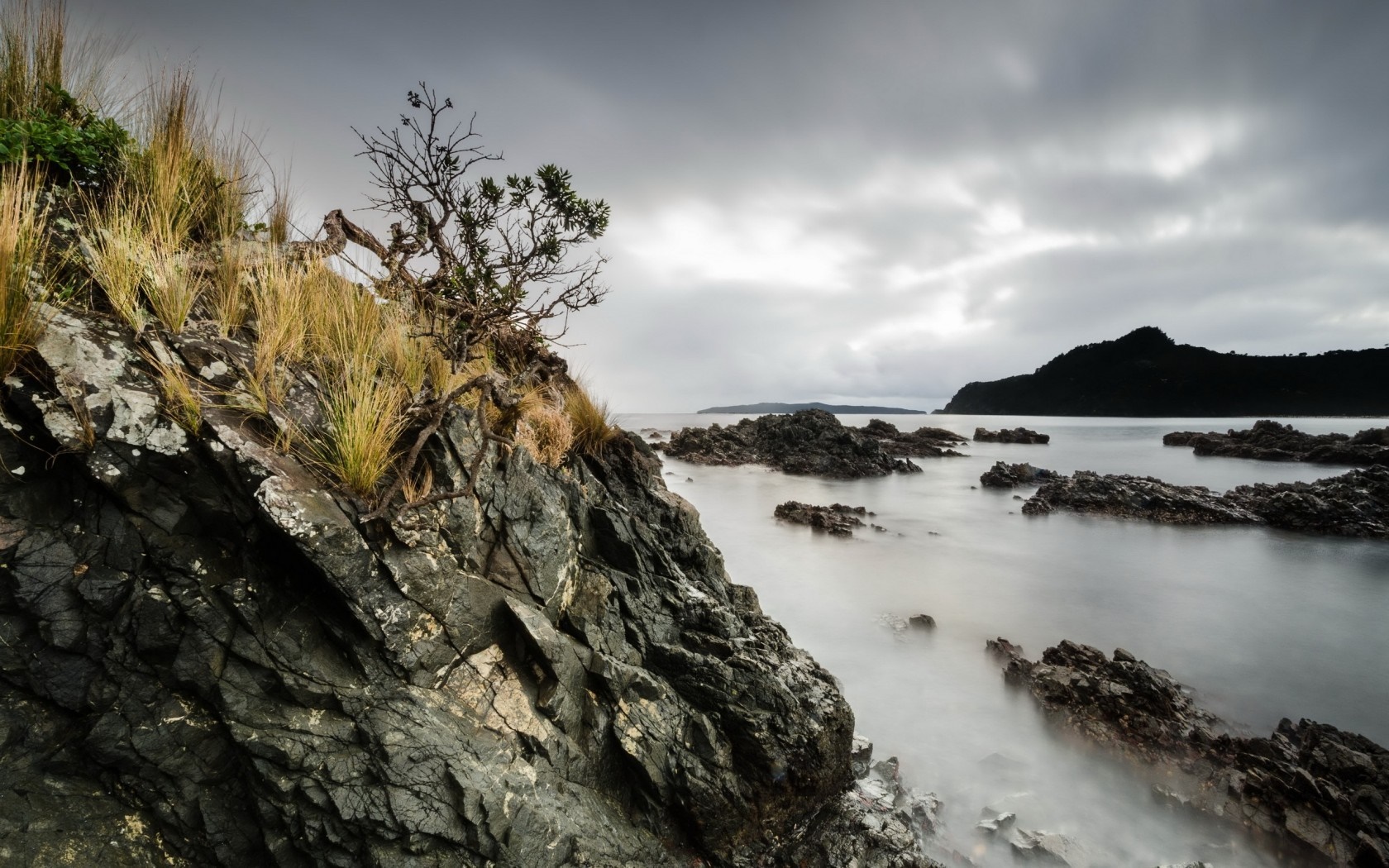 Rocky coast with calm sea under cloudy sky HD Wallpaper