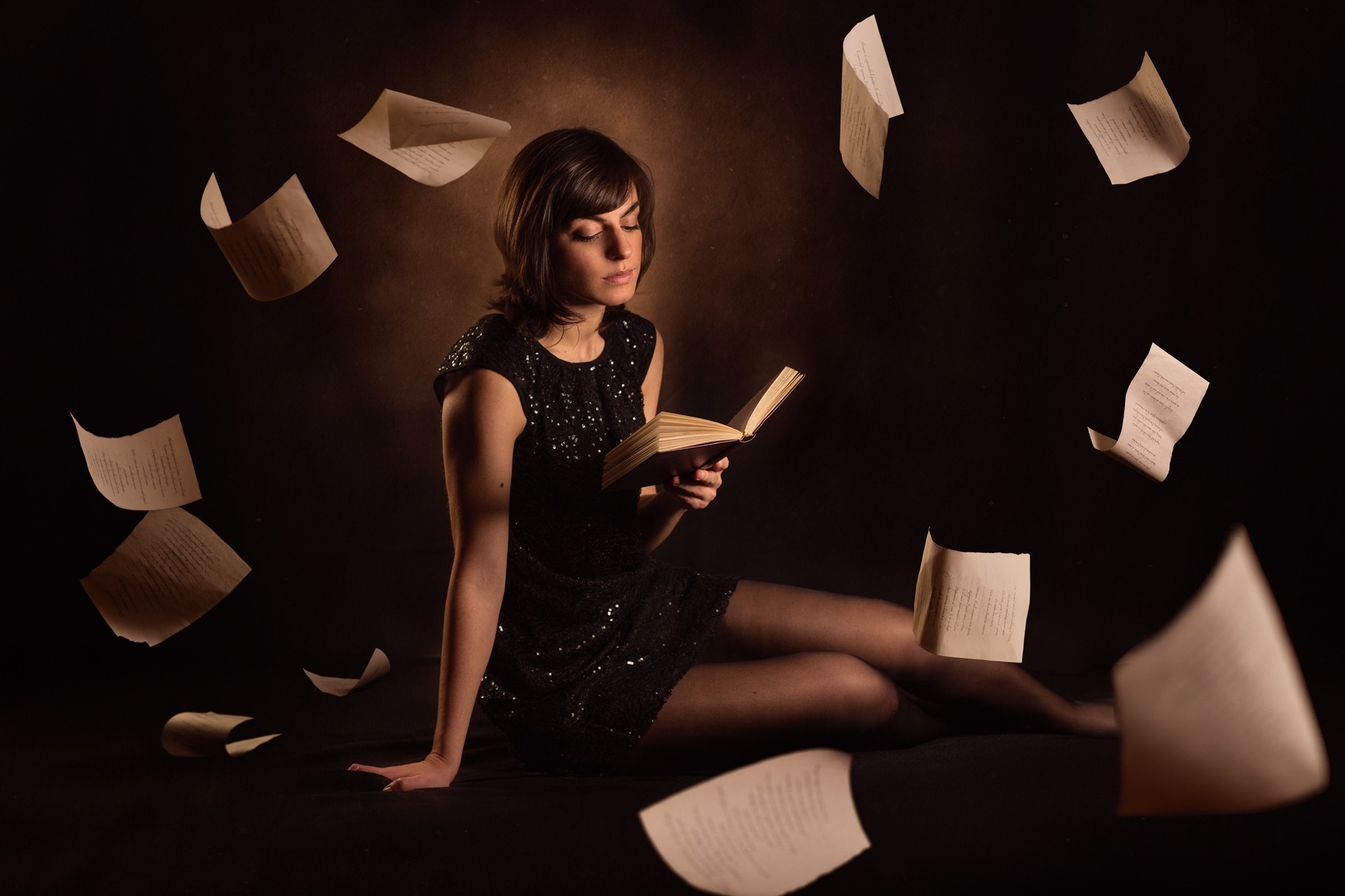 Woman in black dress reading a book with papers flying HD Wallpaper