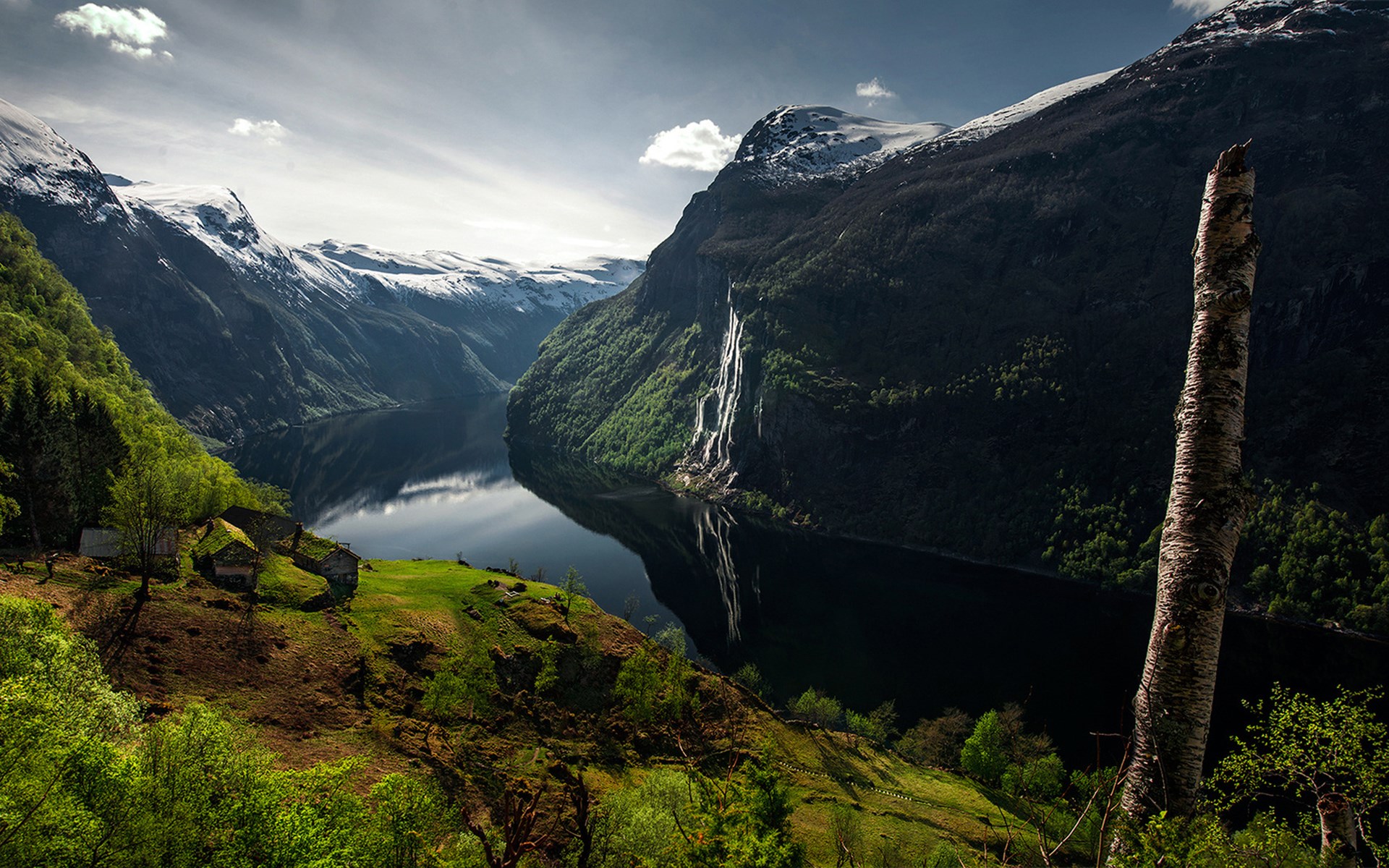 Waterfall cascading into a Norwegian fjord with snow-capped mountains HD Wallpaper
