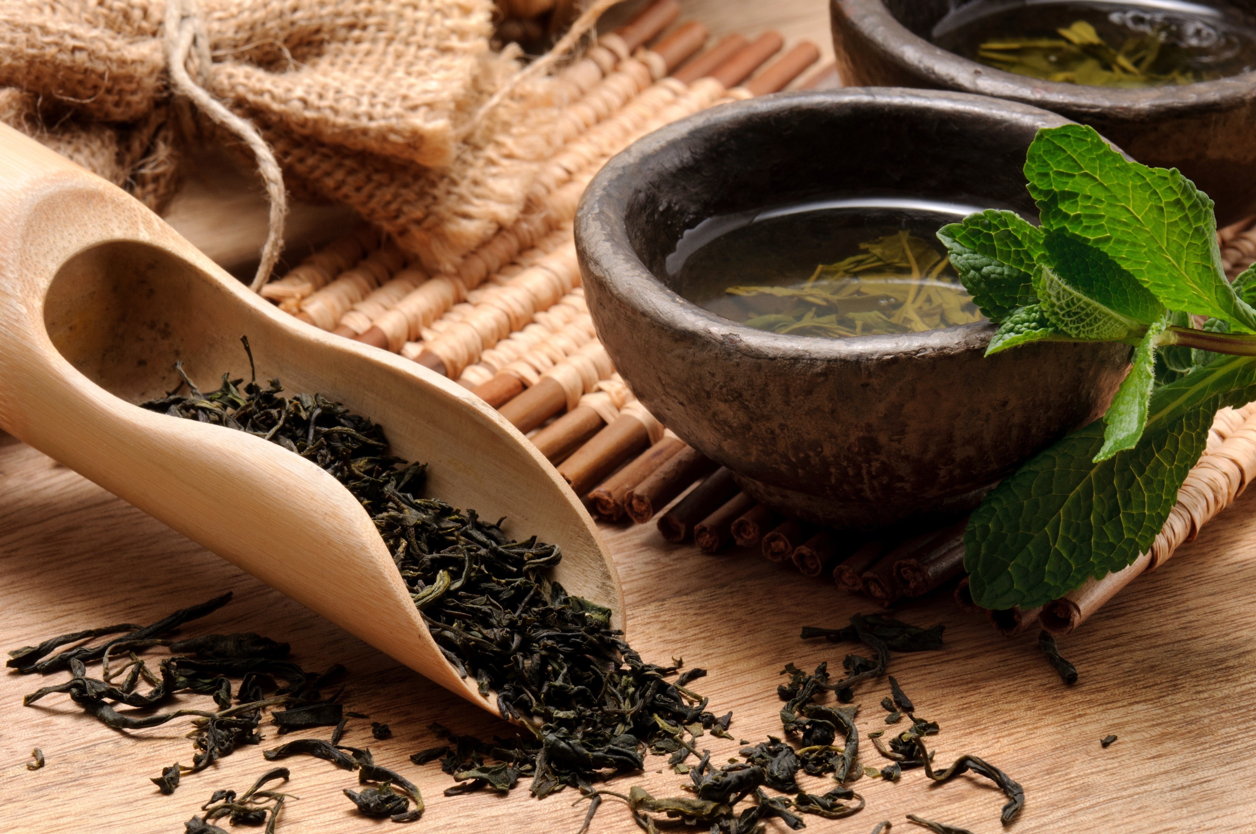 Green tea leaves in a wooden scoop with tea in bowls HD Wallpaper