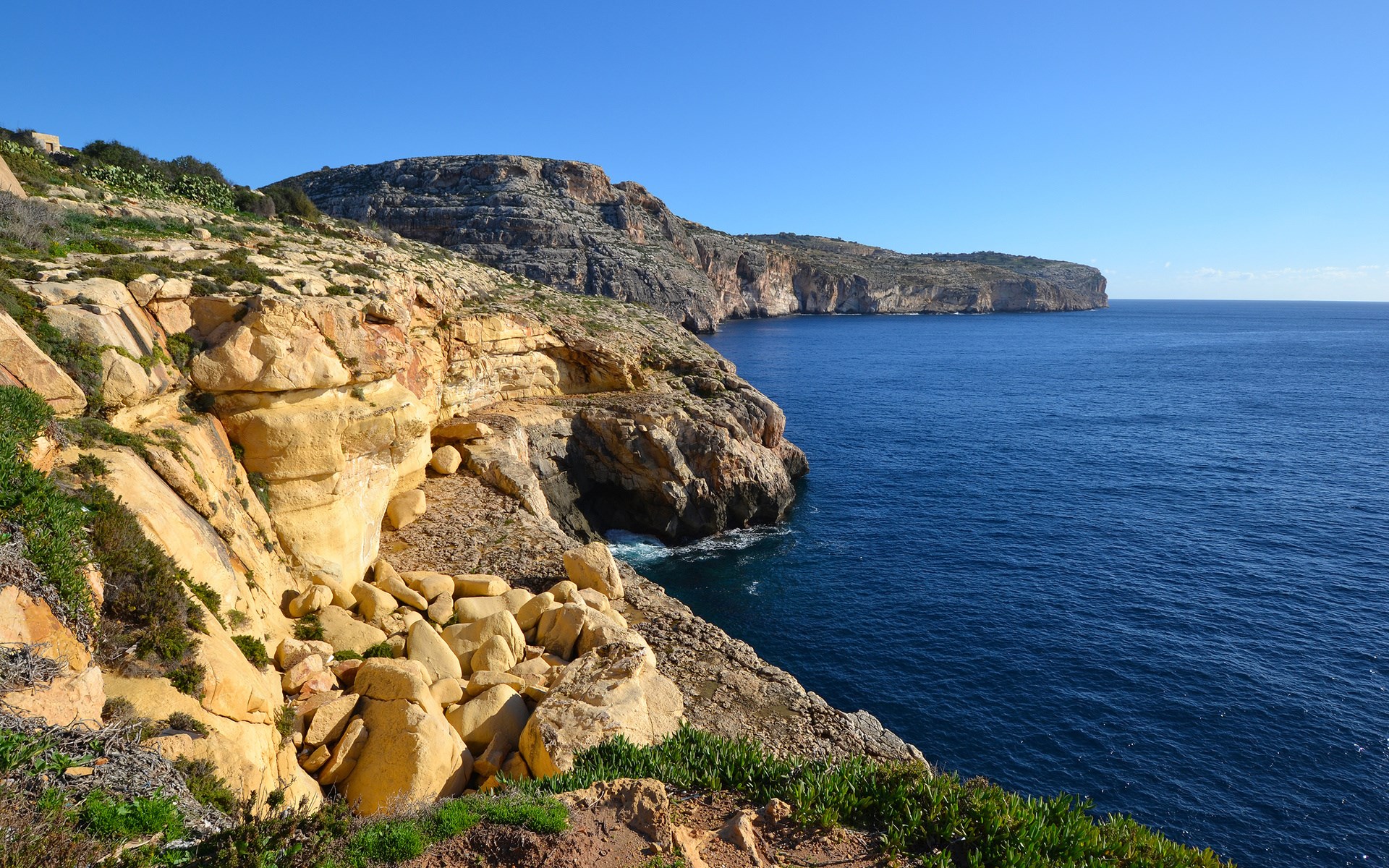 Rocky coastline overlooking the blue sea under a clear sky HD Wallpaper