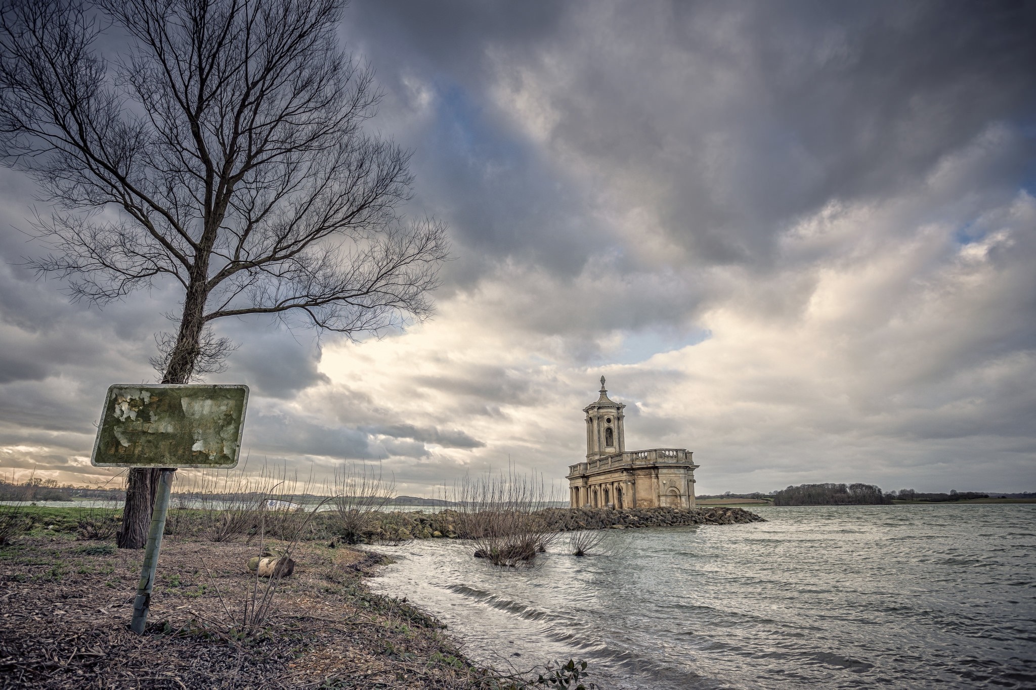Building on a rocky outcrop in a lake under a cloudy sky HD Wallpaper