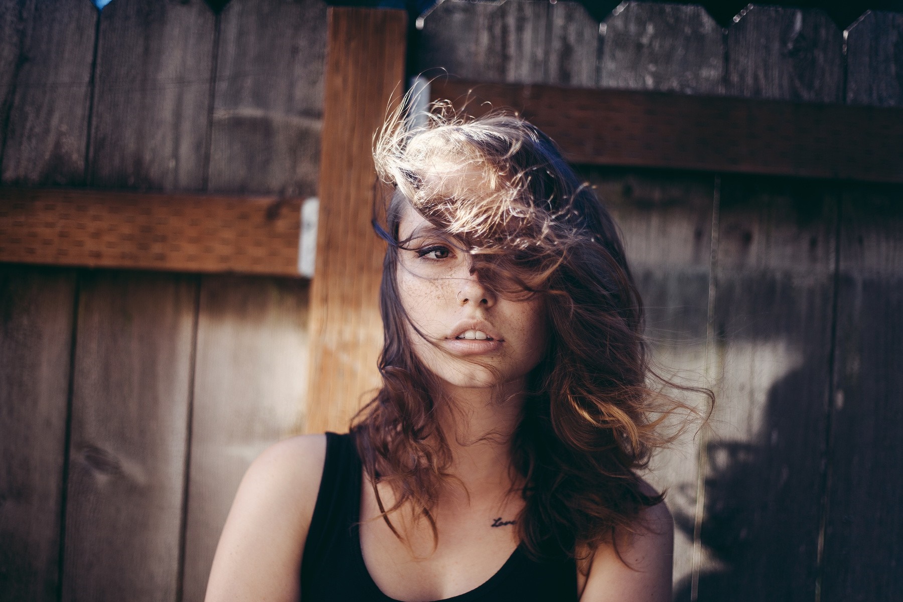 Woman with hair blowing in face in front of a wooden fence HD Wallpaper