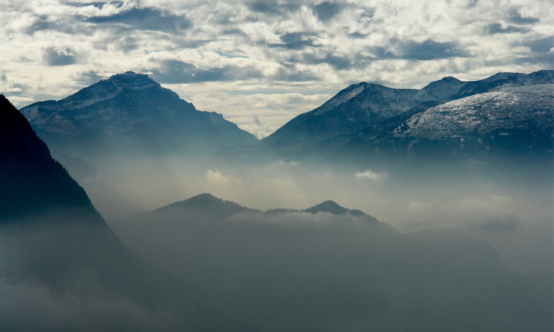 Misty mountains with snow-capped peaks under a cloudy sky HD Wallpaper