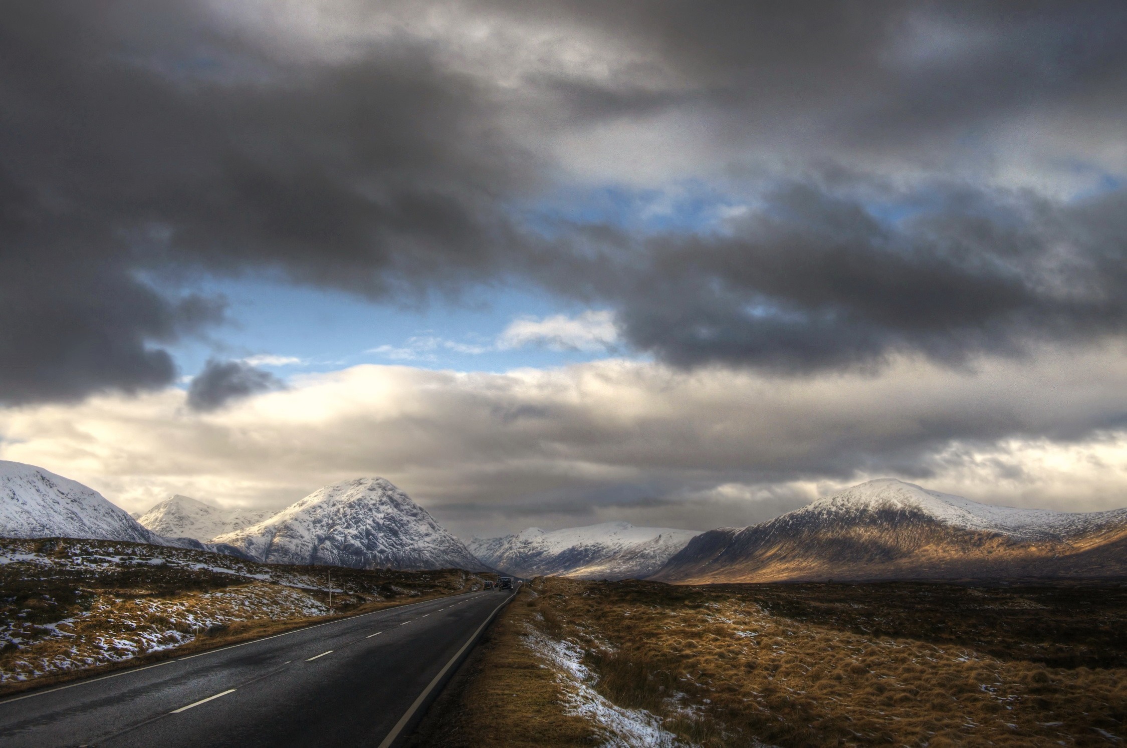 Road through snowy mountains in Scotland under dramatic clouds HD Wallpaper
