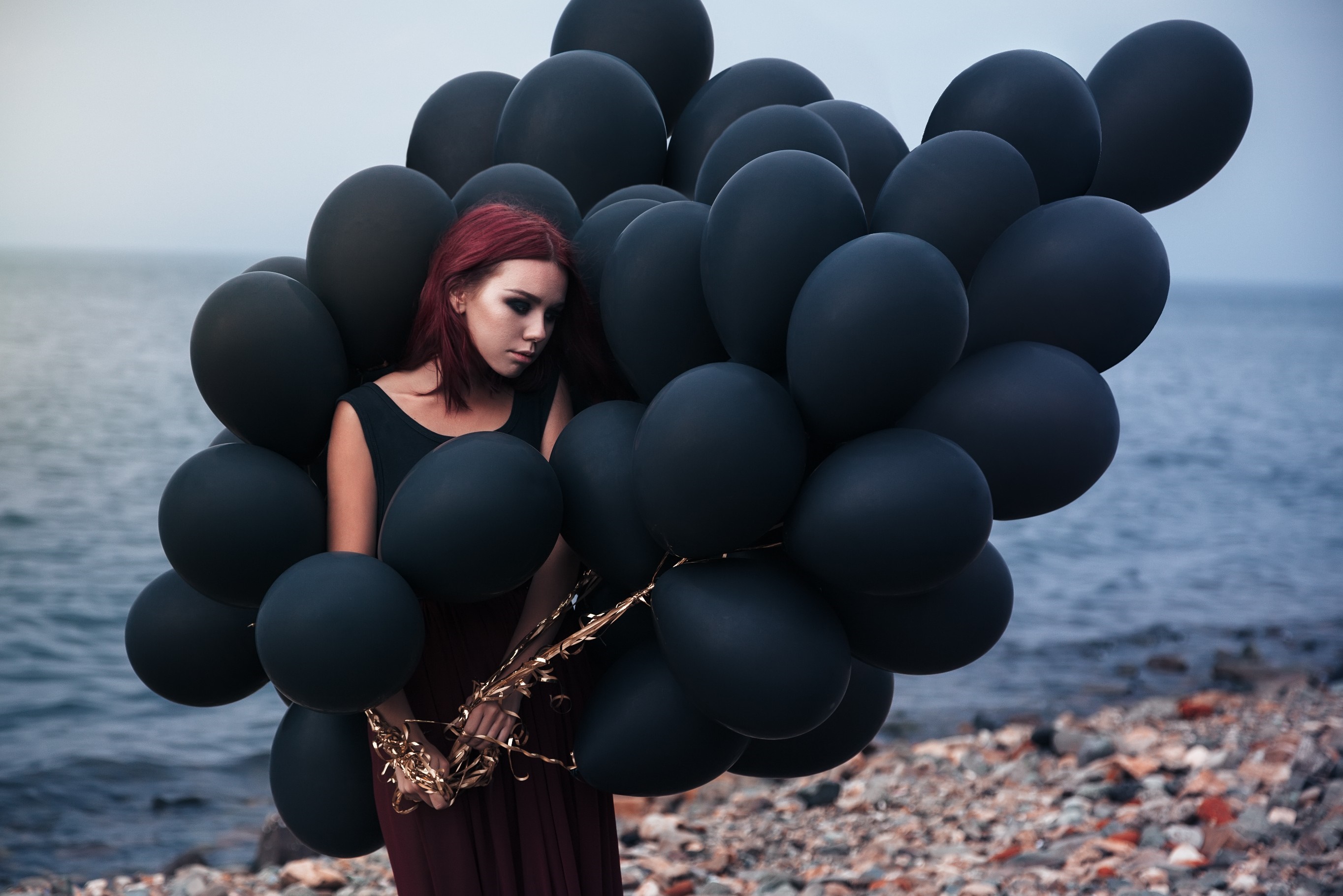 Woman with black balloons on a rocky beach HD Wallpaper