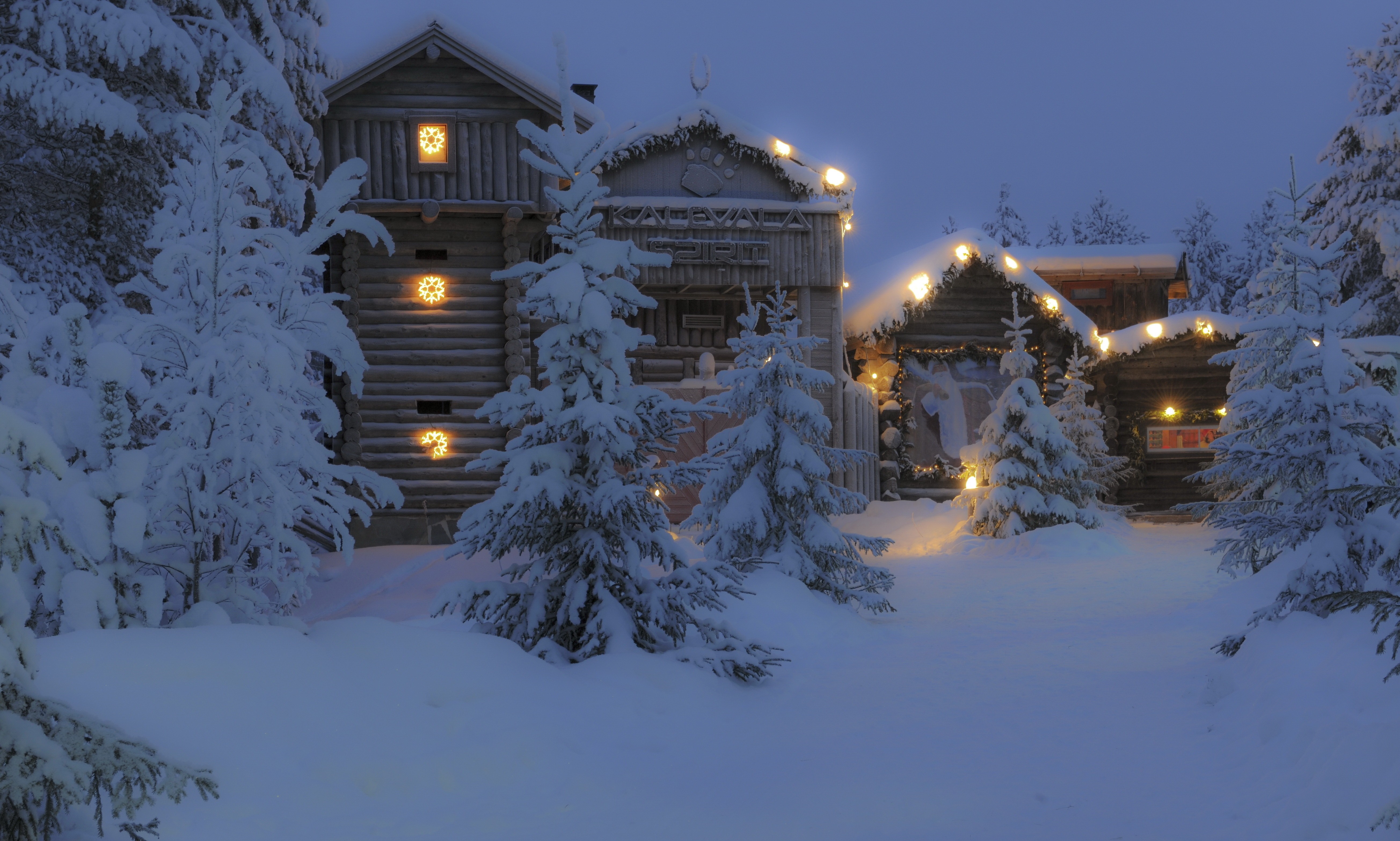 Snowy log cabins decorated with Christmas lights in a forest HD Wallpaper