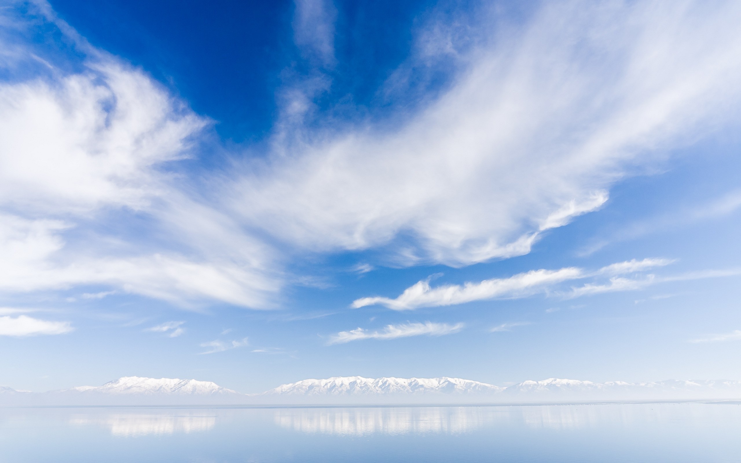 Snow-capped mountains reflected in a calm body of water under a cloudy sky HD Wallpaper