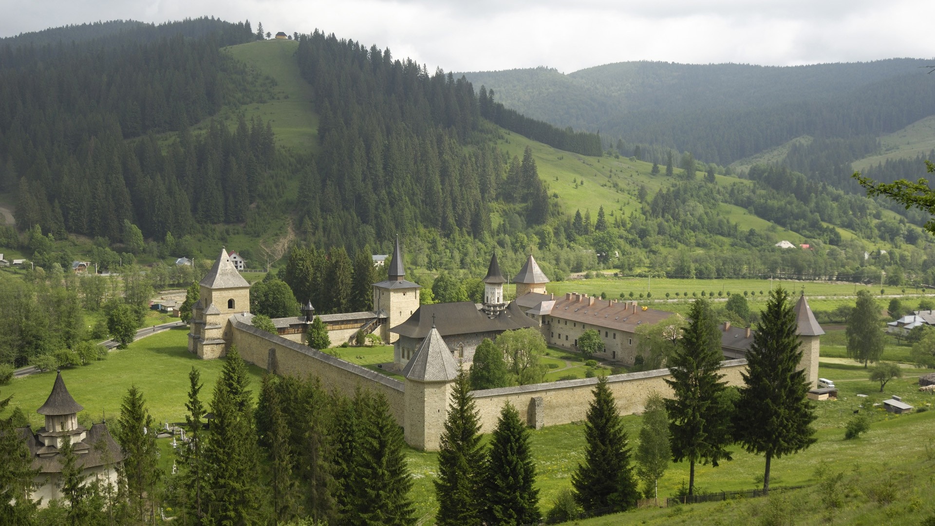 Monastery in a valley with forested hills HD Wallpaper