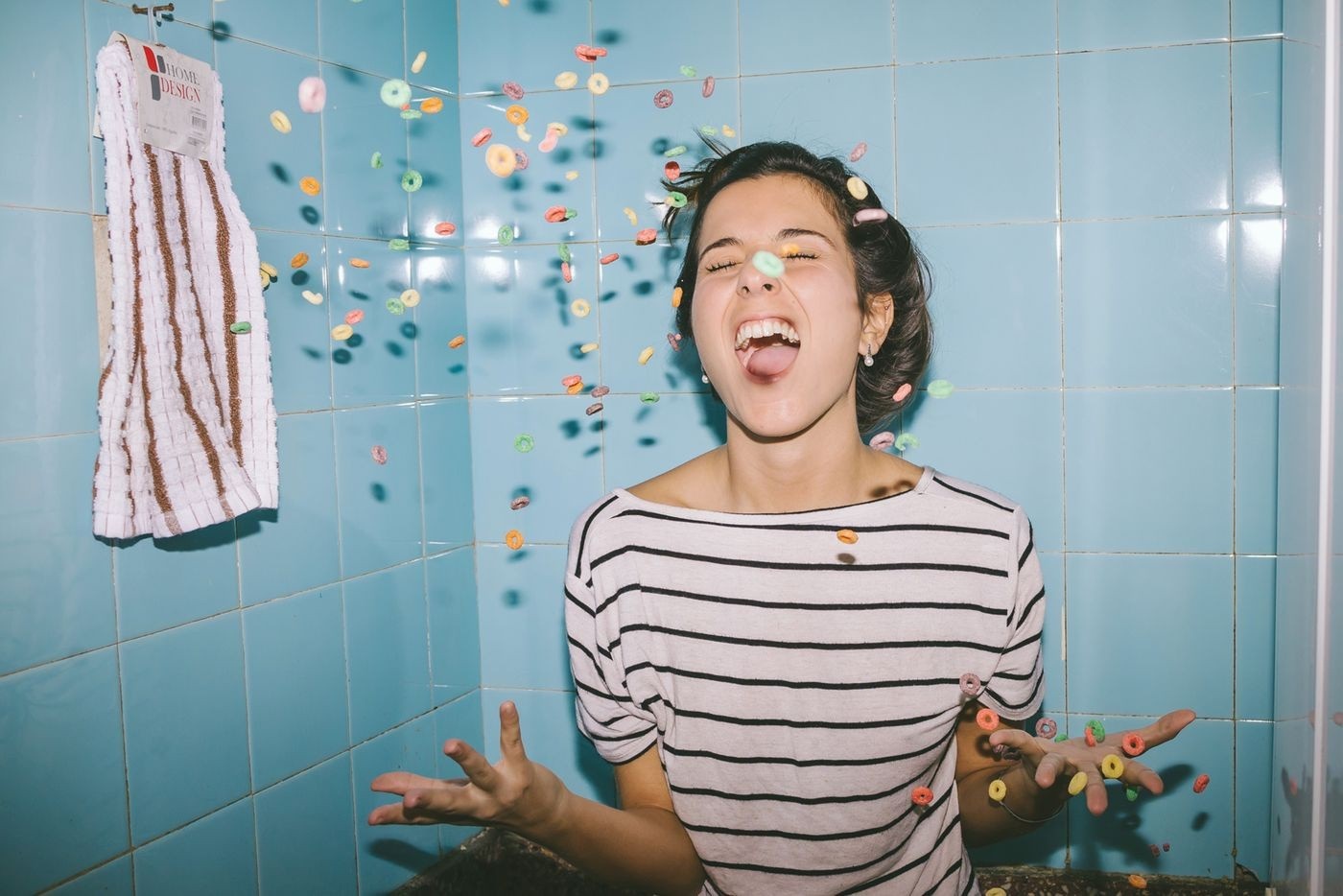 Woman throwing colorful cereal in a blue tiled room HD Wallpaper