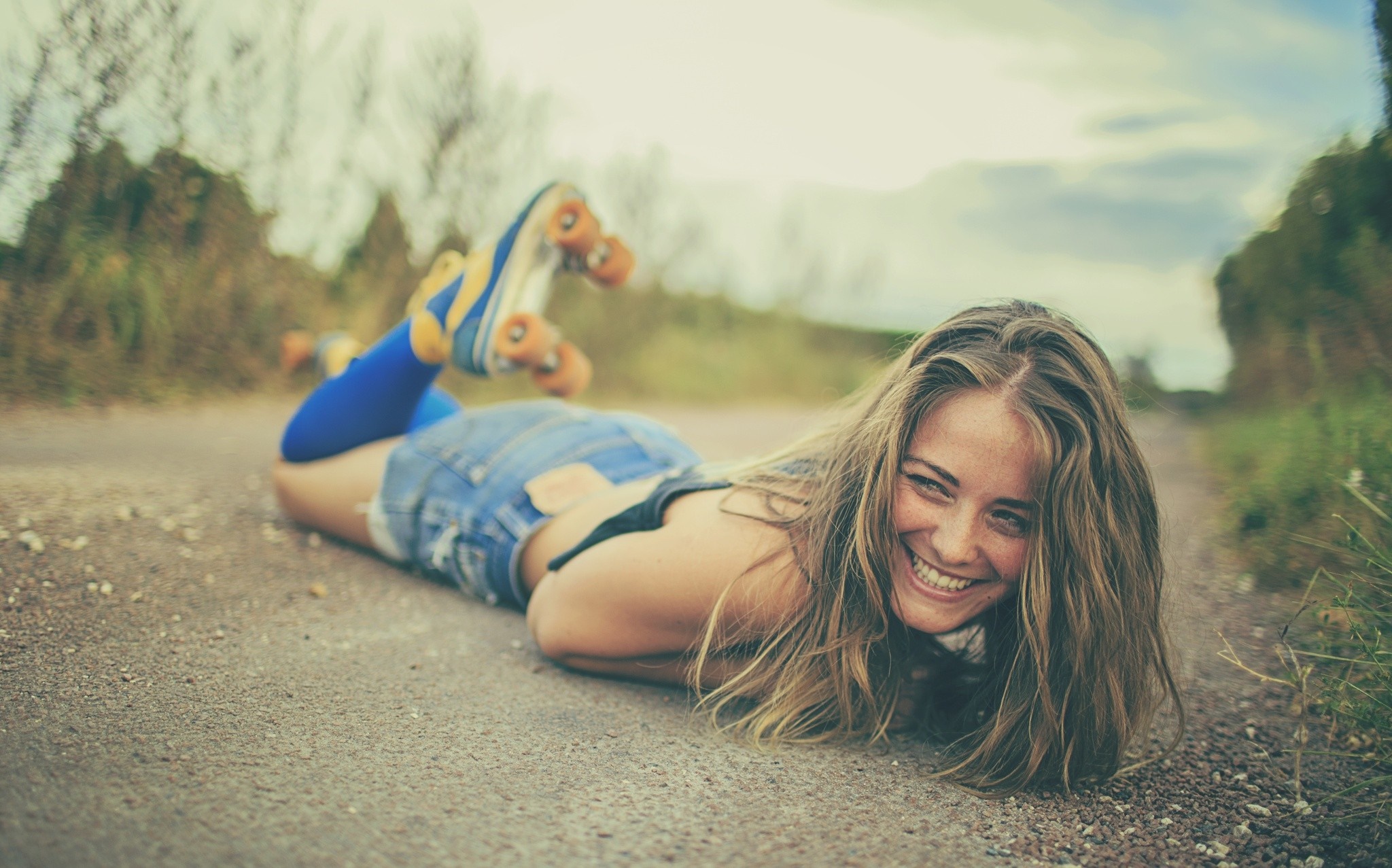 Woman in jean shorts and roller skates lying on a road HD Wallpaper