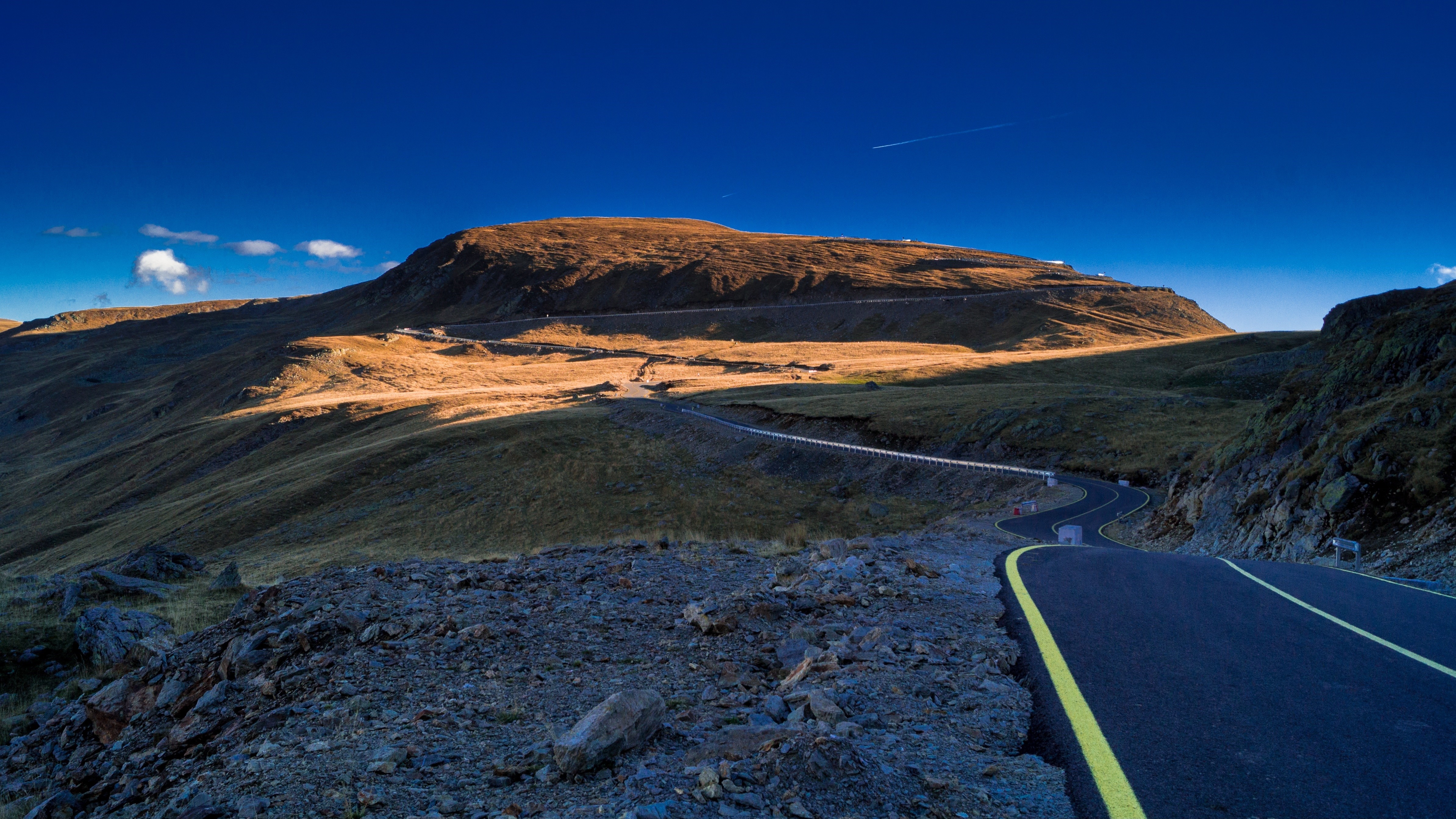 Mountain road winding through a golden landscape under a blue sky HD Wallpaper