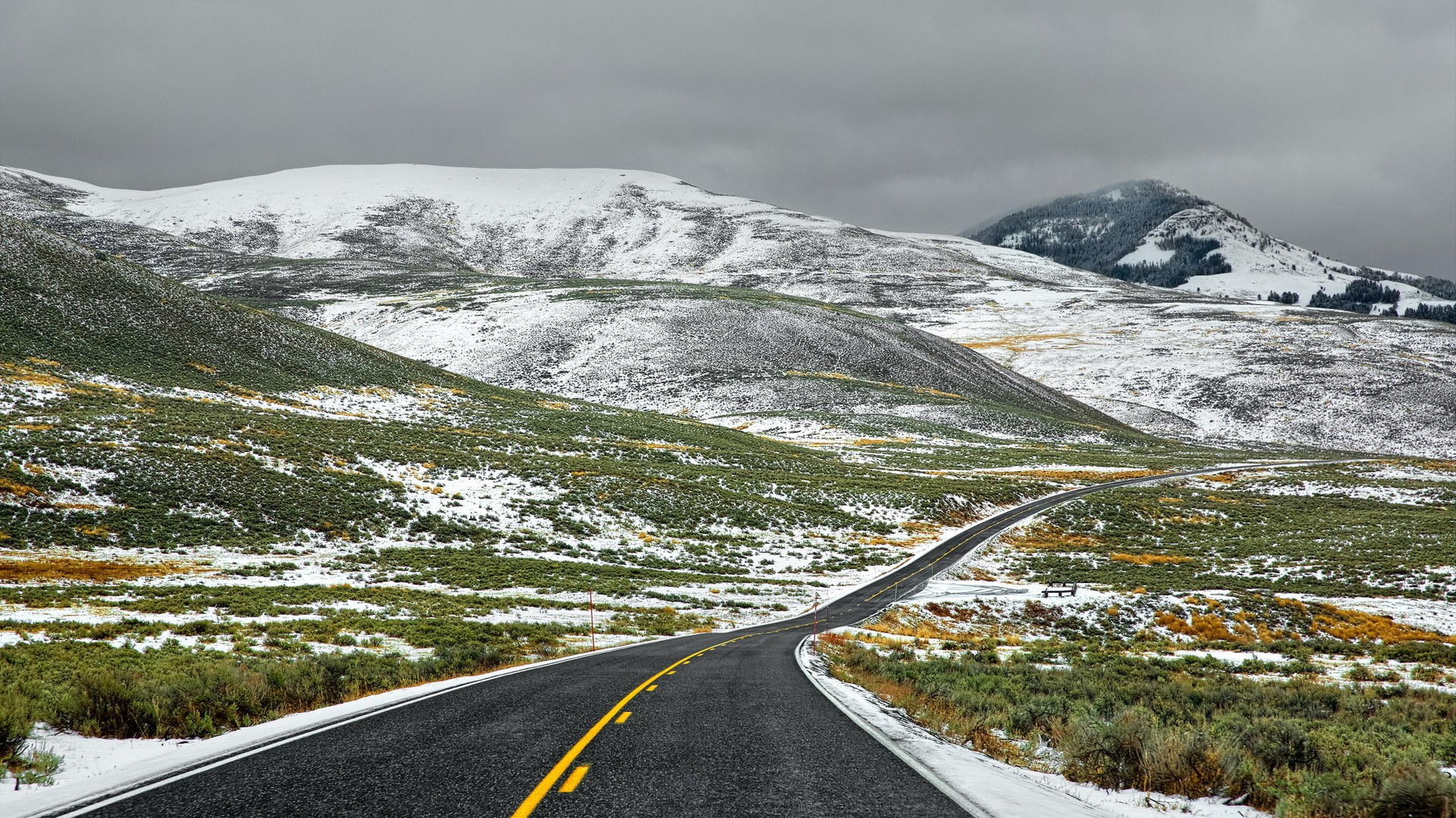 Winding road through snow-dusted hills under cloudy sky HD Wallpaper