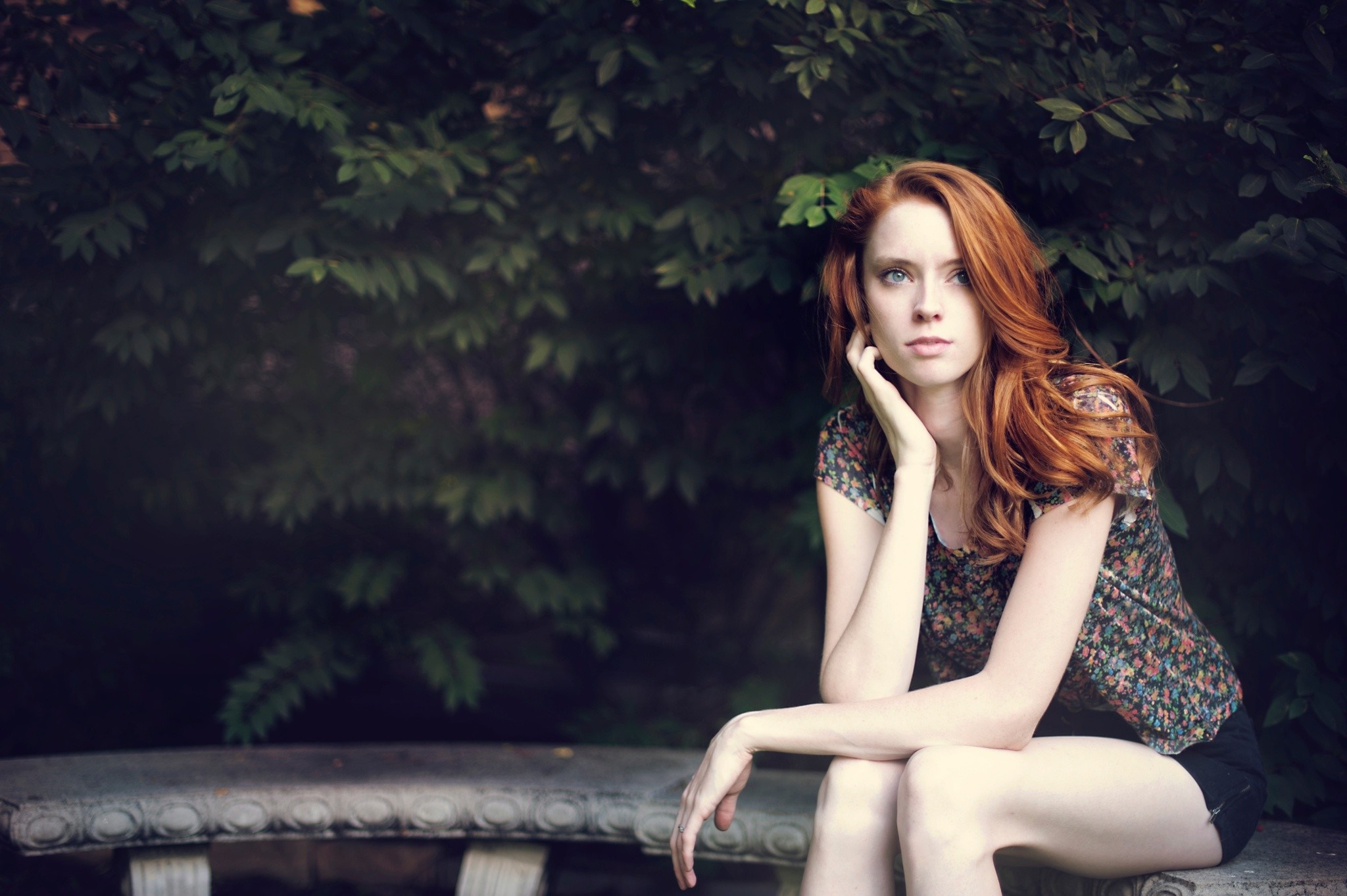 Redhead woman sitting on a stone bench in front of foliage HD Wallpaper