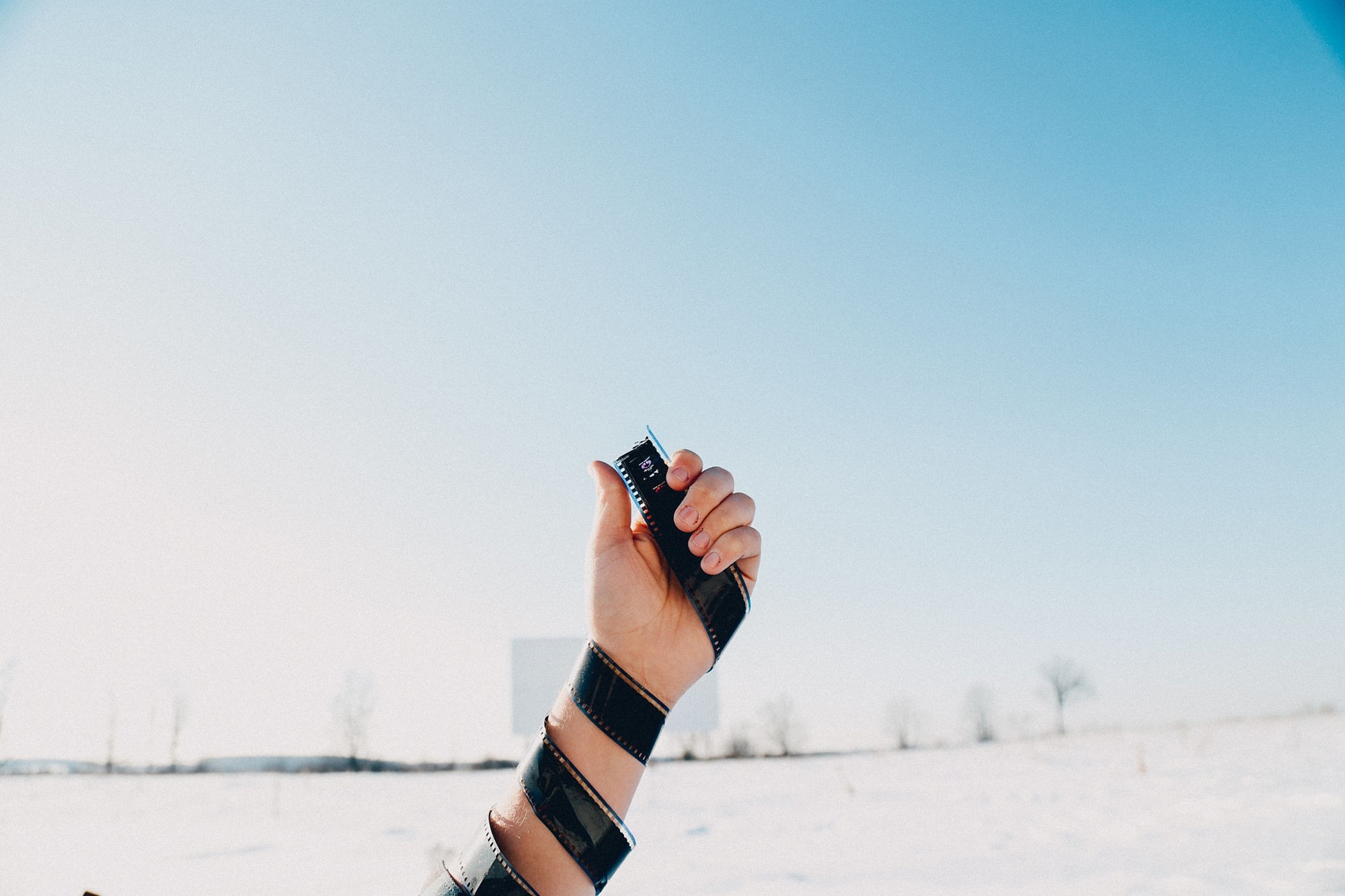 Hand holding film reel in snowy landscape HD Wallpaper