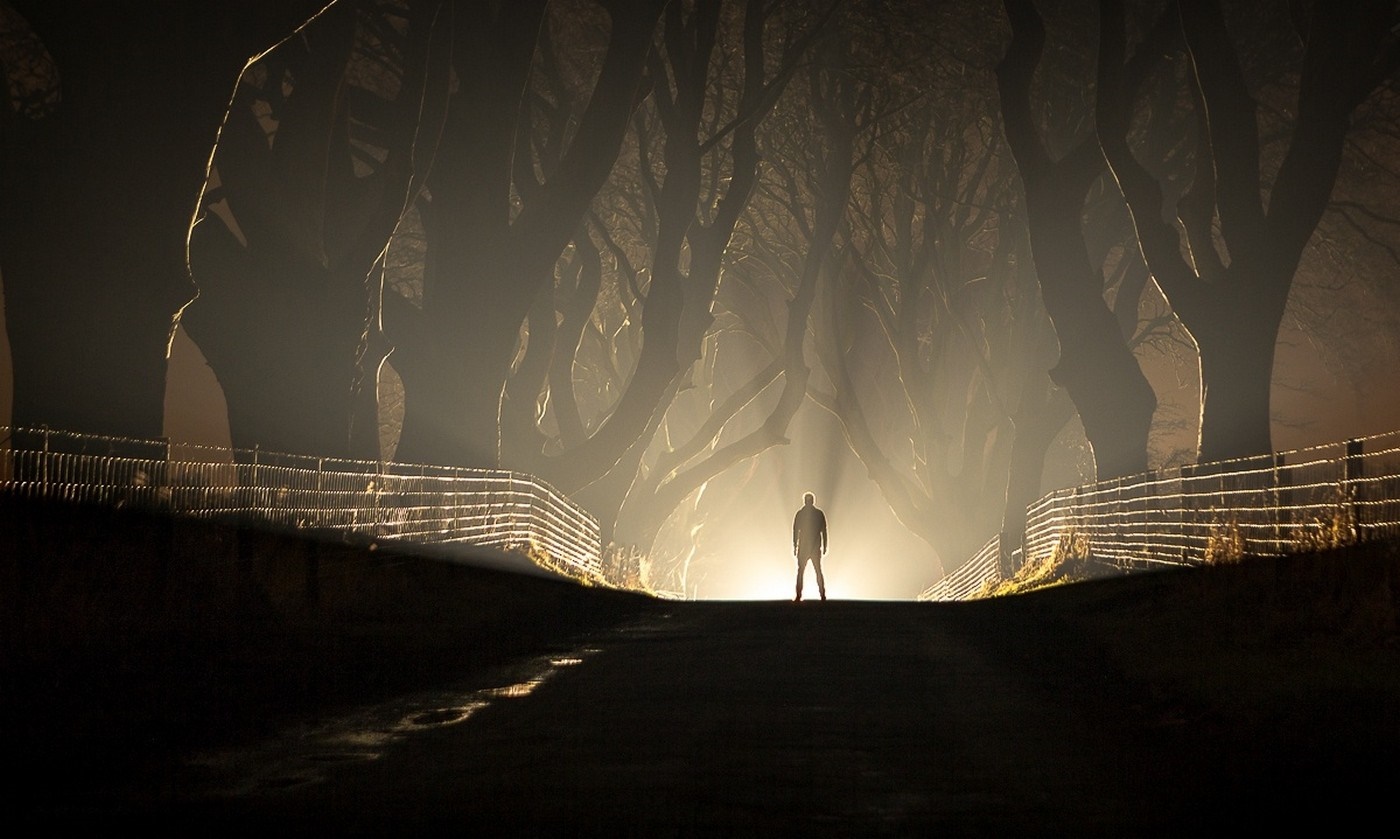Man standing on a road at night with trees and mist HD Wallpaper