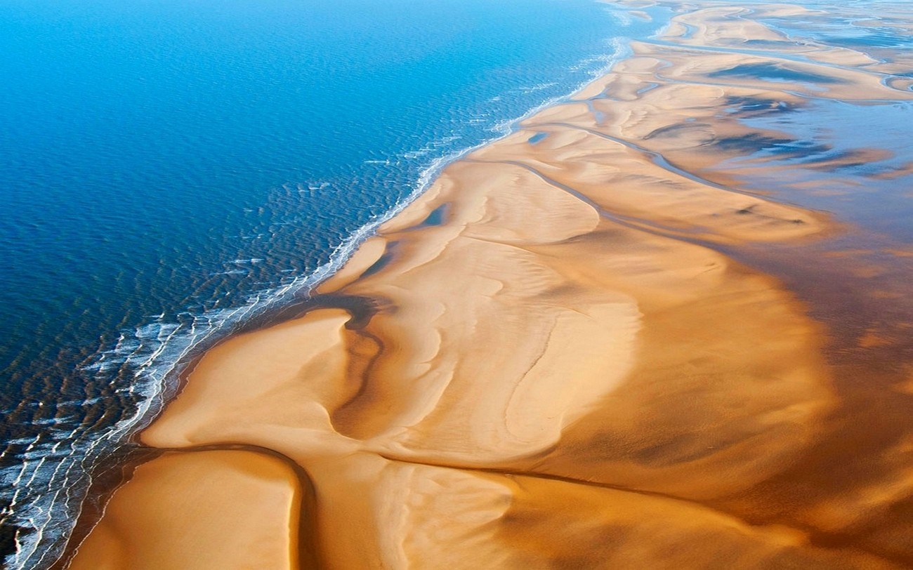 Aerial view of a sandy coastline with blue ocean waves HD Wallpaper