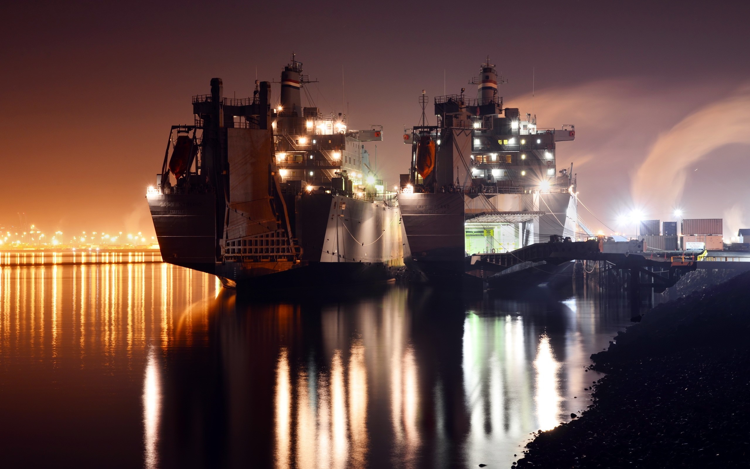 Two large ships docked at night with city lights in the background HD Wallpaper