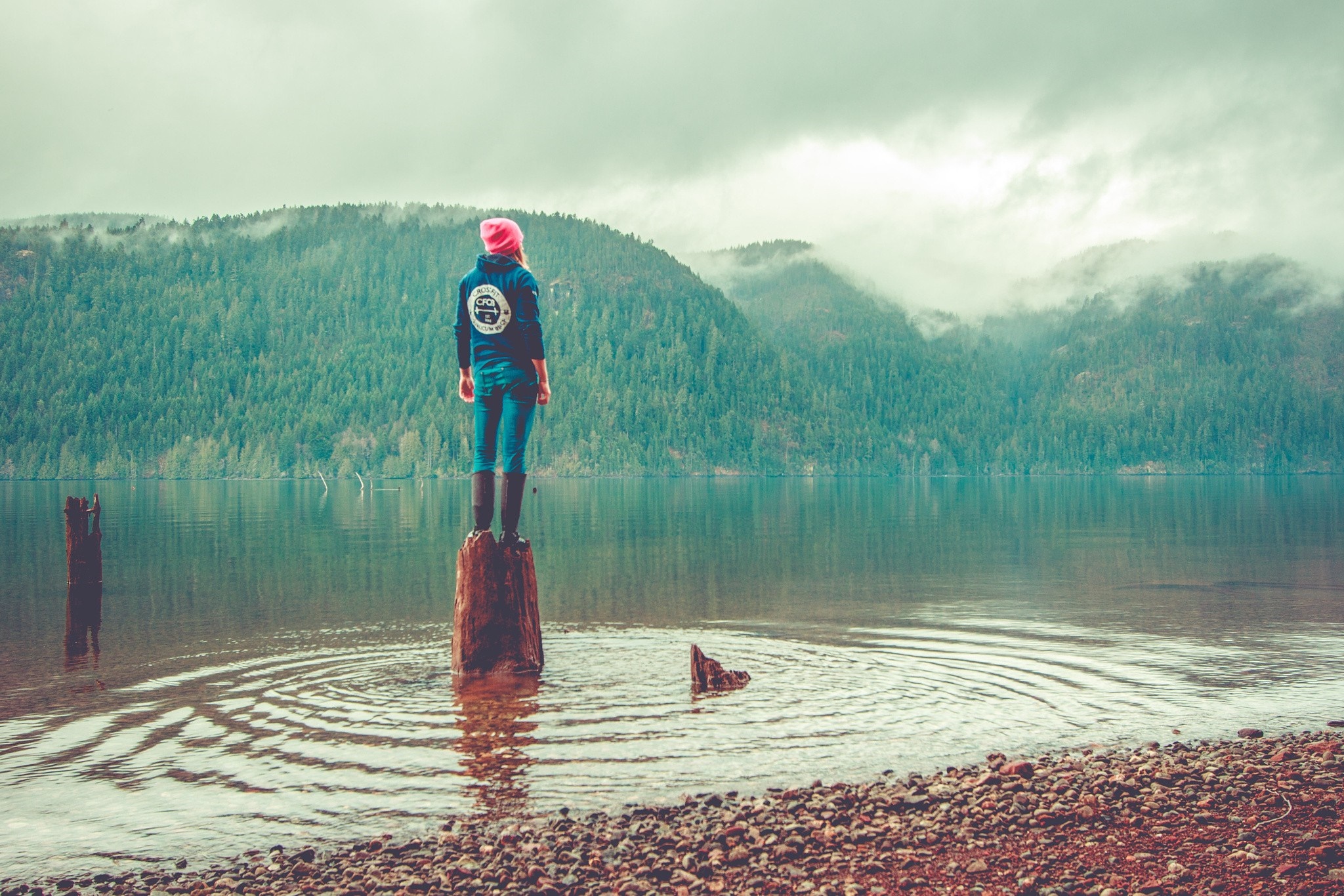 Woman standing on a log in a lake with mountains HD Wallpaper