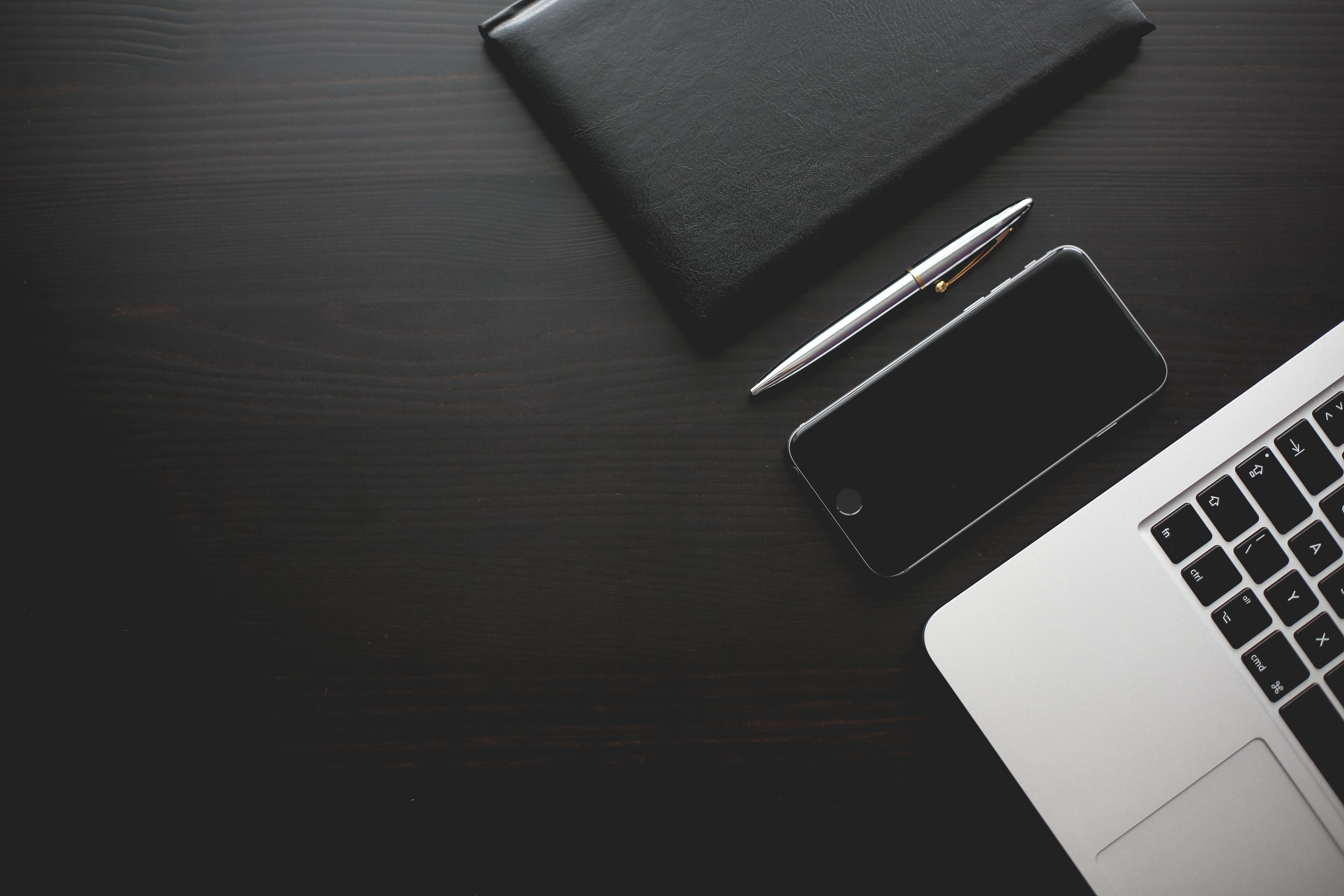 Laptop, smartphone, pen, and notebook on a dark wooden desk HD Wallpaper