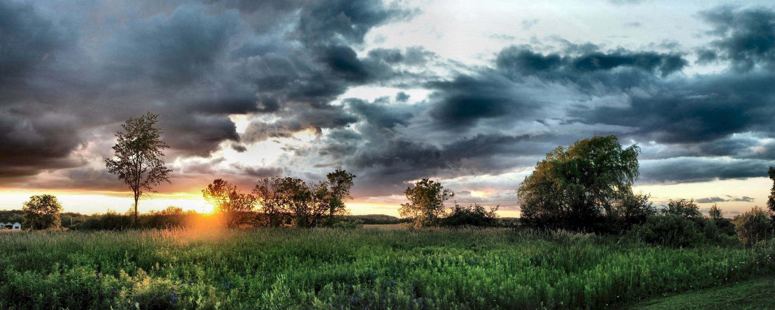 Sunset over a grassy field with dramatic clouds HD Wallpaper