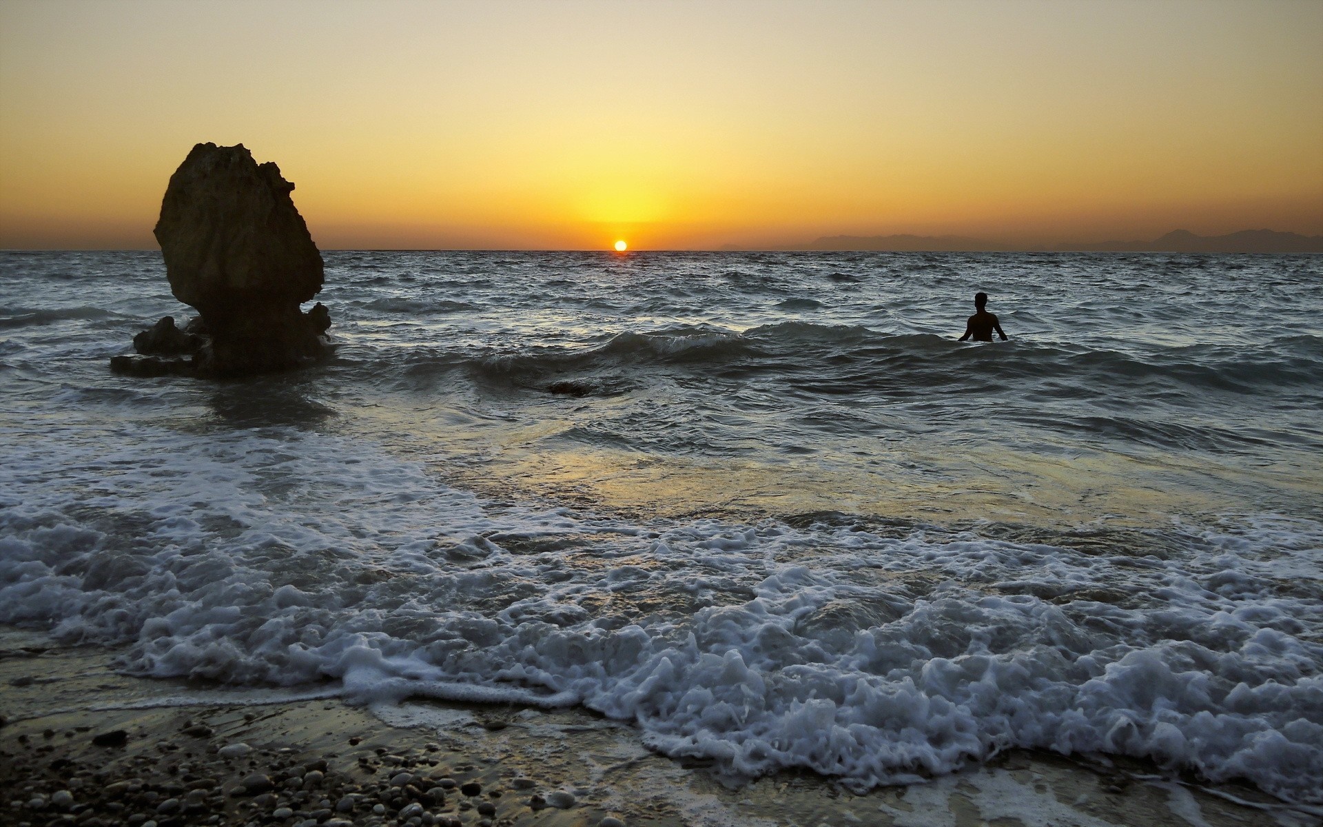 Person swimming in the sea at sunset with rock formation HD Wallpaper