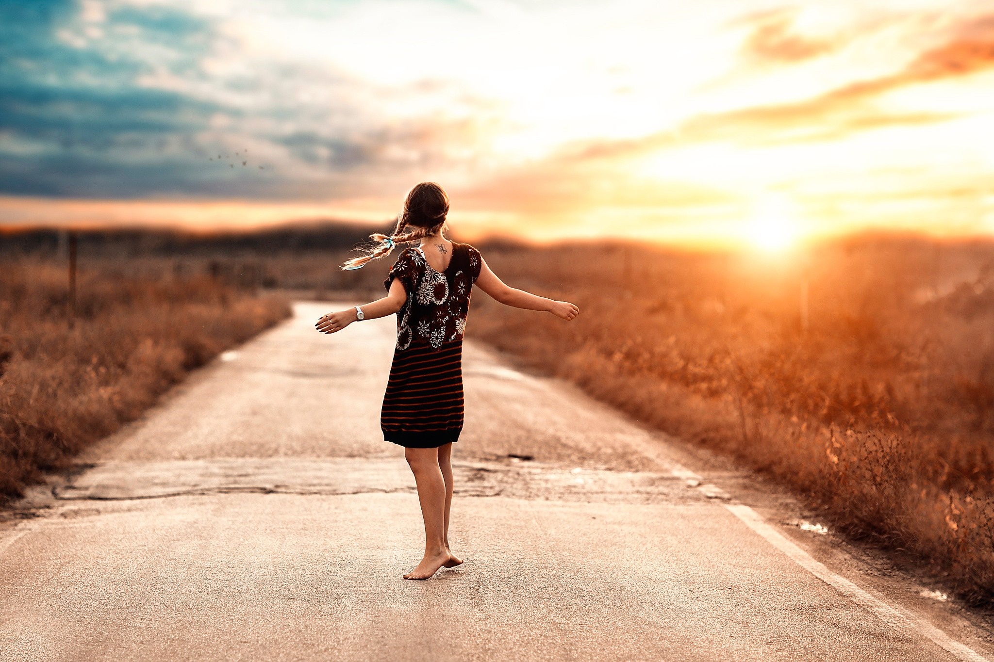 Woman with braided hair walking on a road at sunset HD Wallpaper