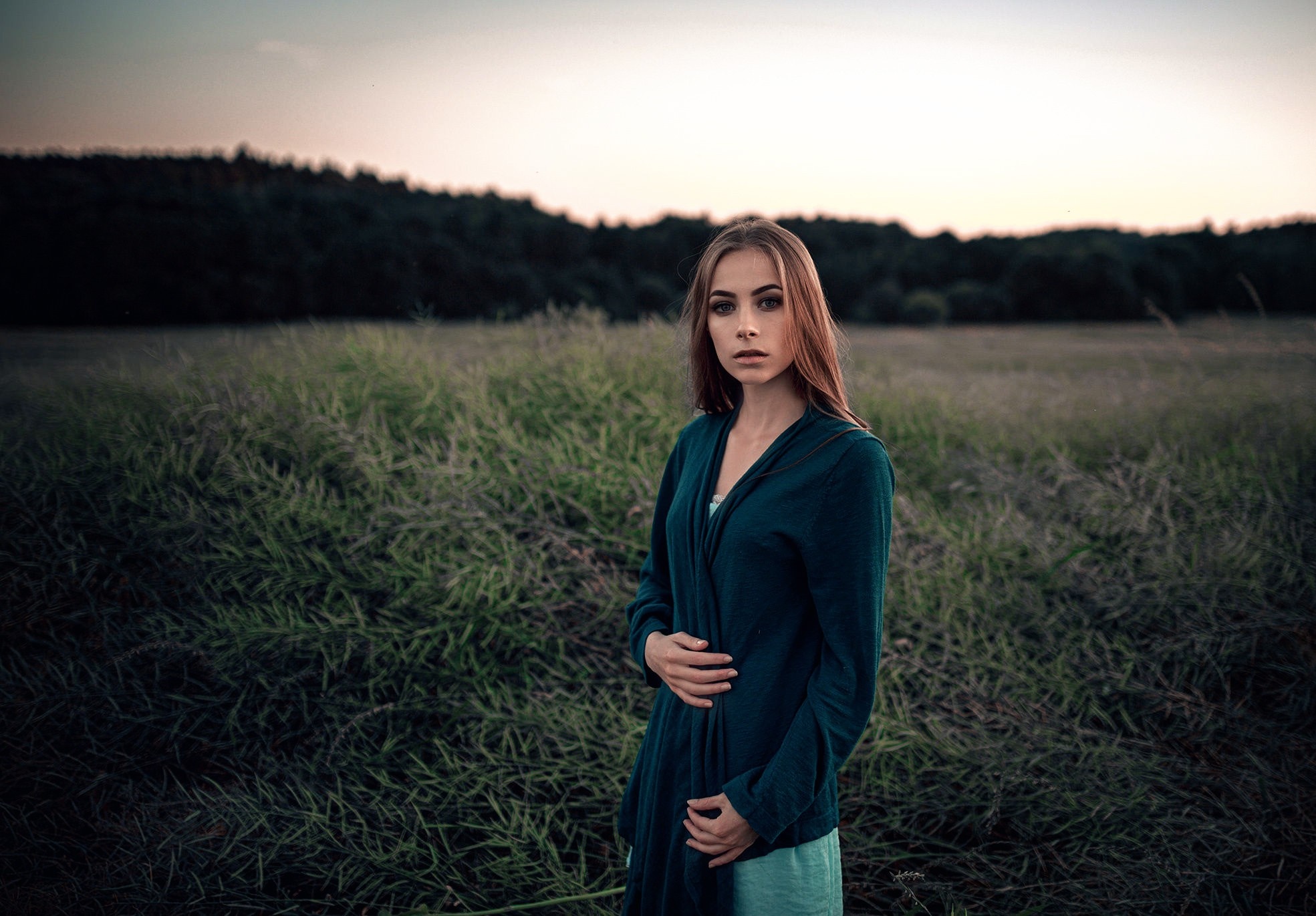 Woman in a teal cardigan in a grassy field at dusk HD Wallpaper