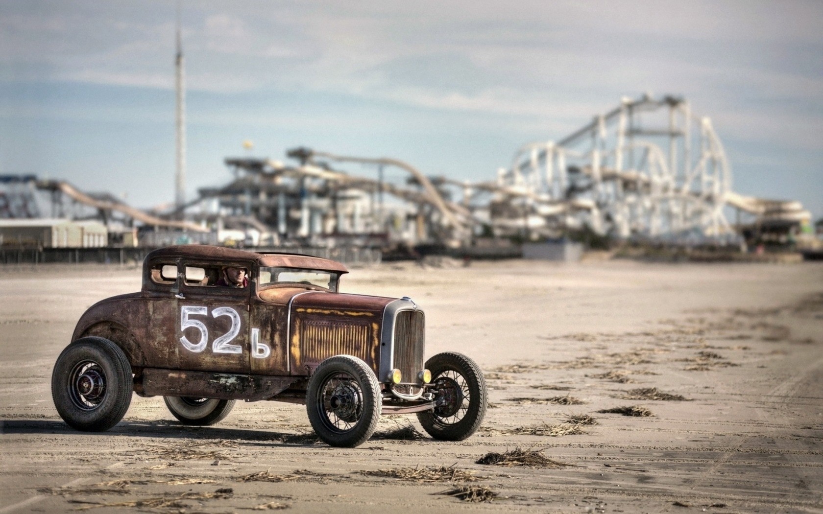 Rusty hot rod car with number 52 on a beach with roller coaster HD Wallpaper