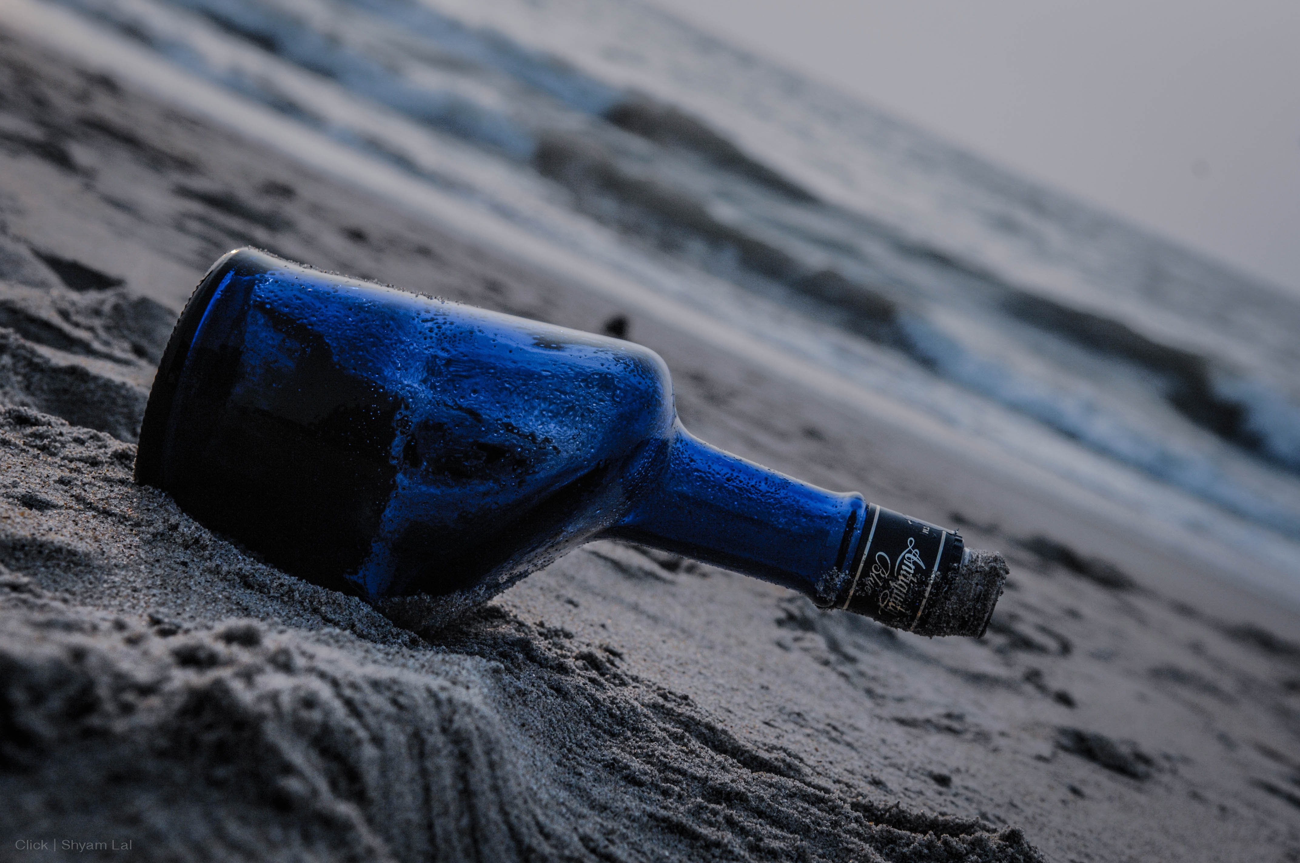 Blue bottle on a sandy beach with waves HD Wallpaper