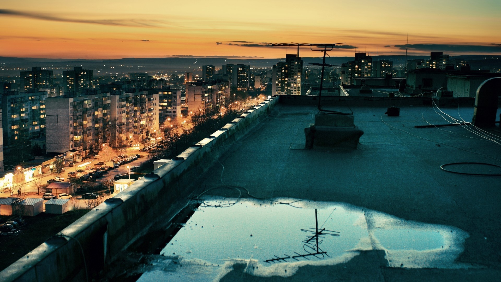 Rooftop view of a city at sunset with a puddle HD Wallpaper