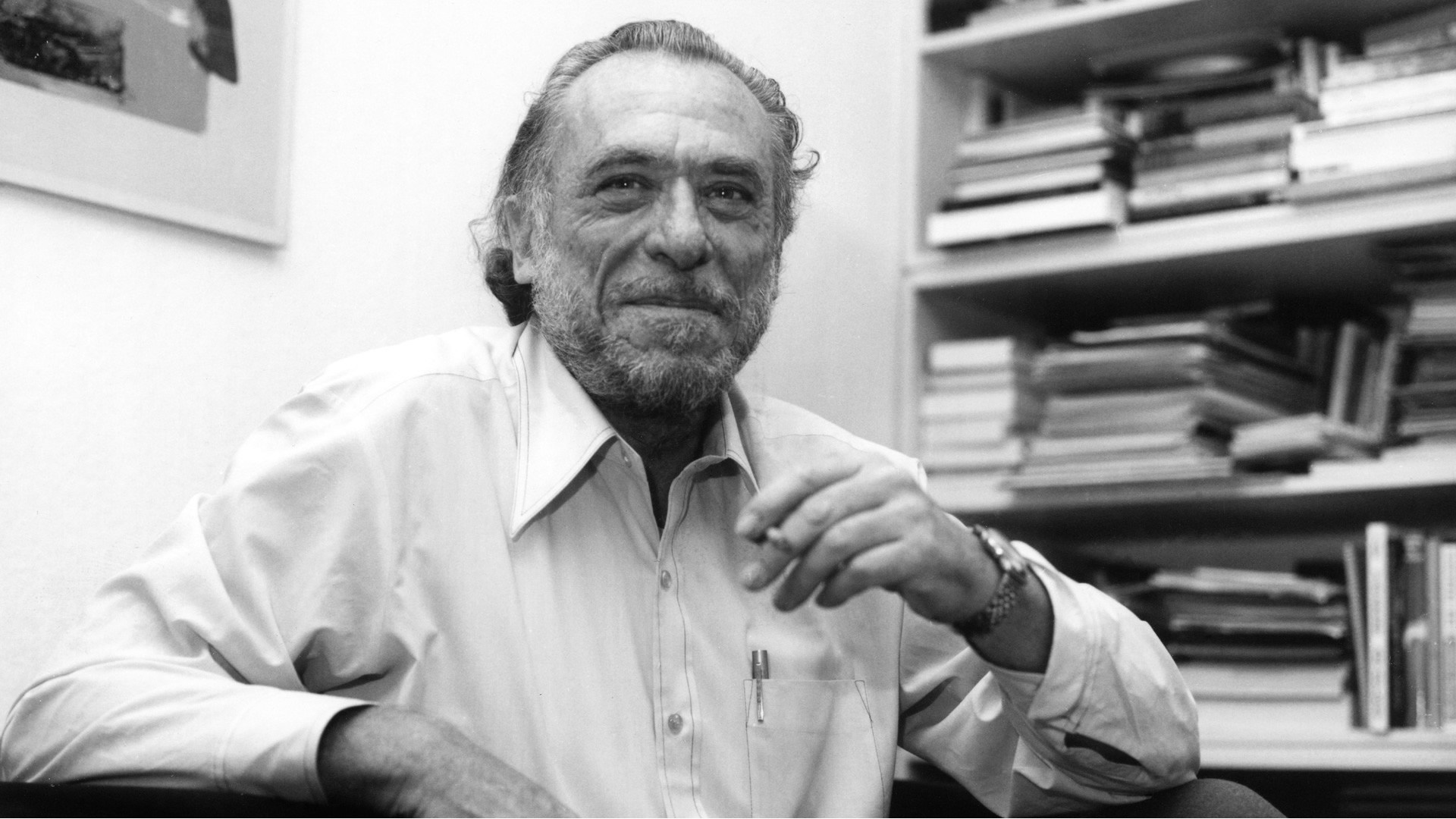Charles Bukowski smoking a cigarette in front of bookshelves HD Wallpaper