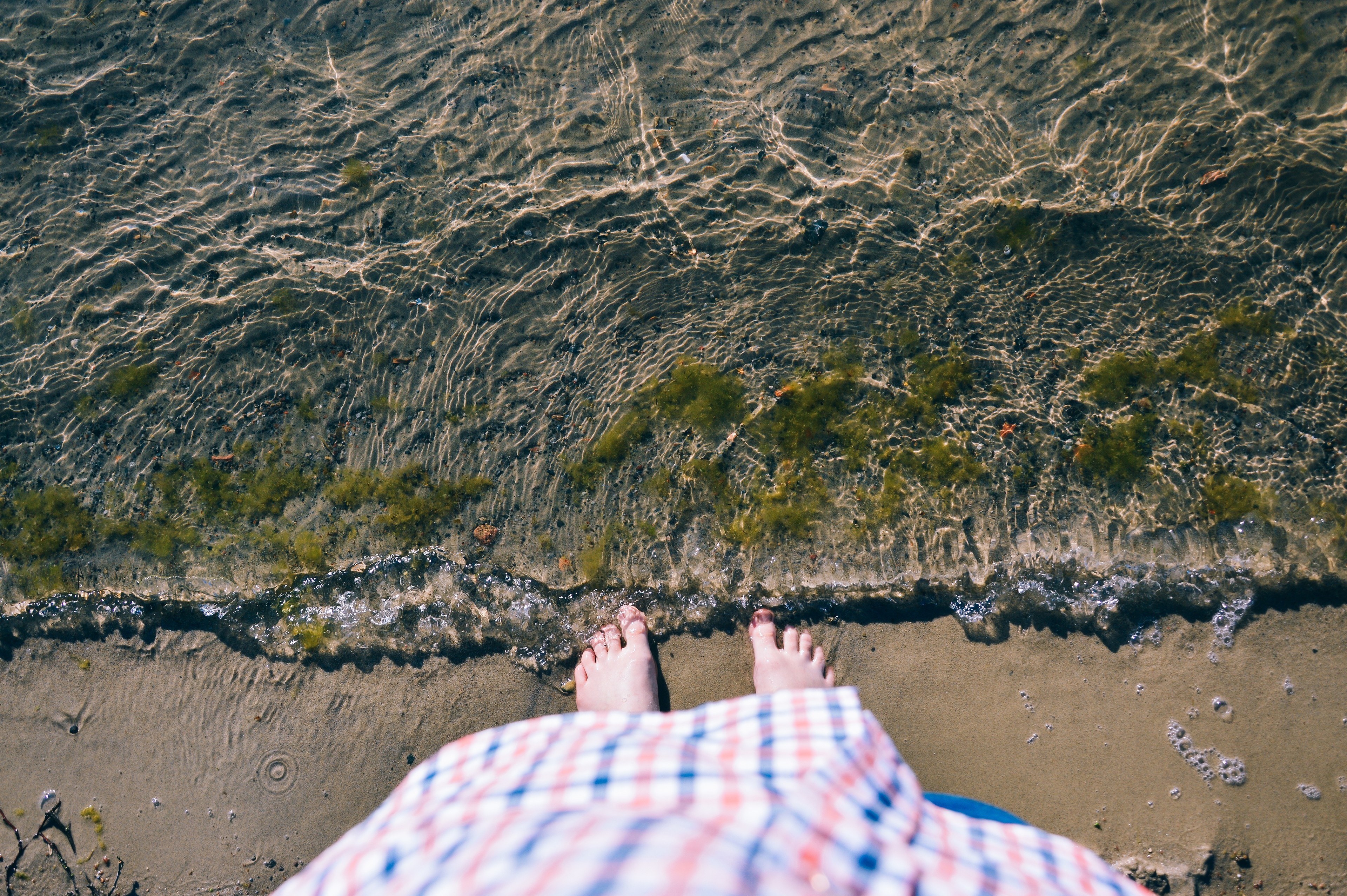 Feet standing at the edge of the water on a sandy shore HD Wallpaper