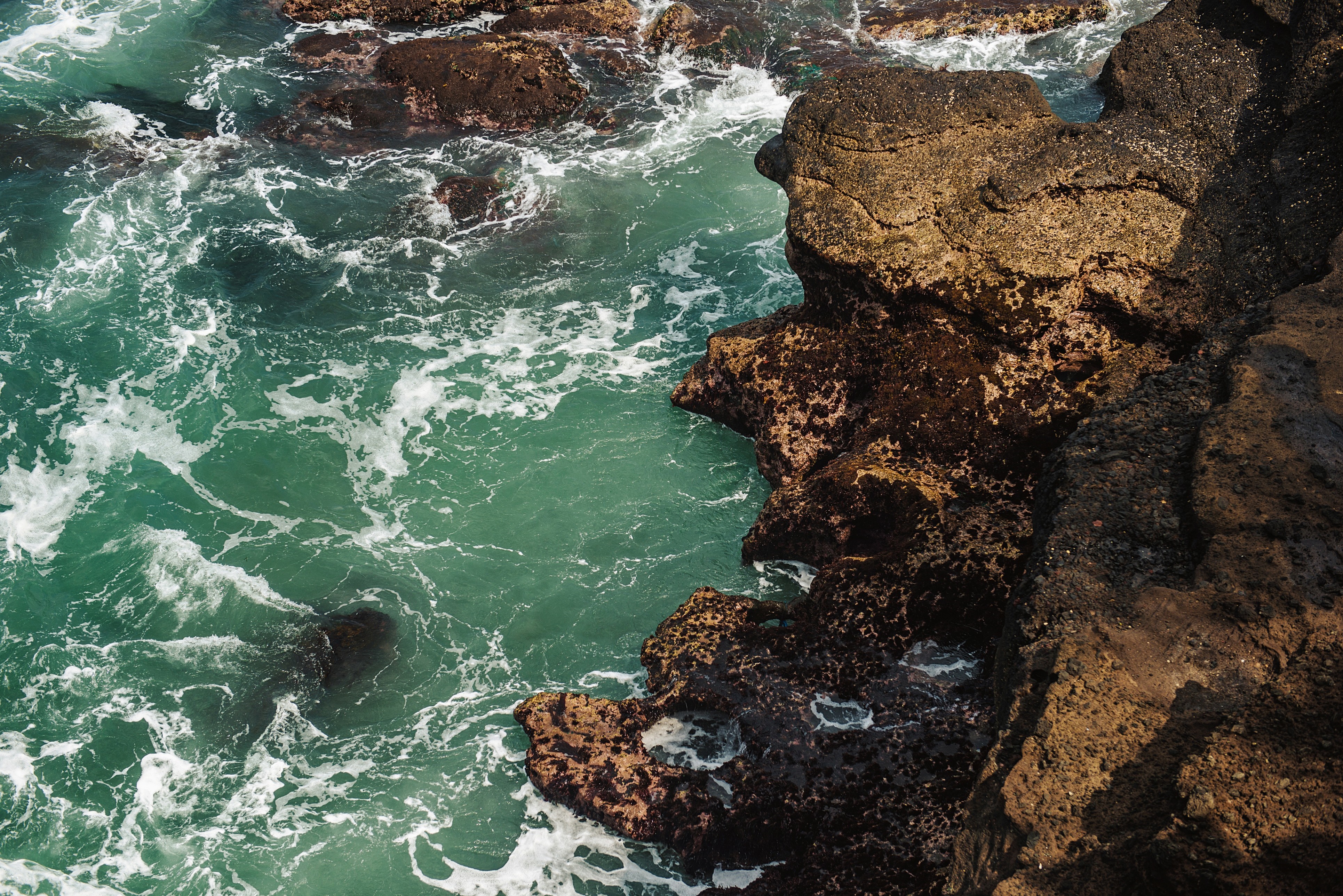 Turquoise ocean waves crashing against dark volcanic rocks HD Wallpaper
