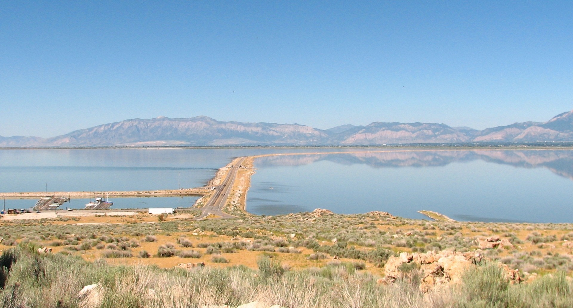 Causeway across a large lake with mountains in the distance HD Wallpaper