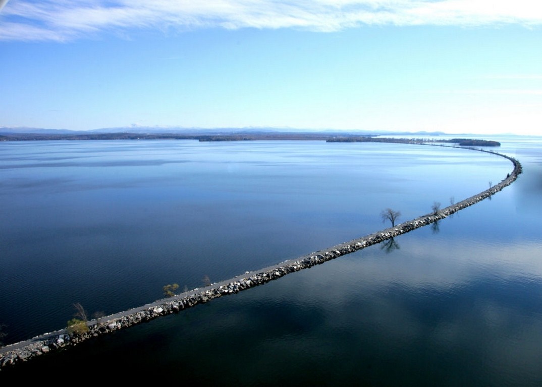Long stone jetty extending into a calm lake with distant mountains HD Wallpaper